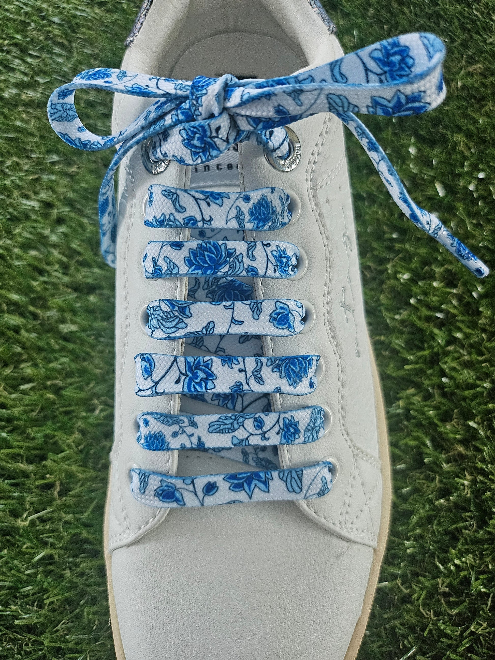 White sneaker with blue floral-patterned laces on a grass background