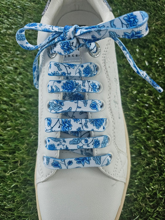 White sneaker with blue floral-patterned laces on a grass background
