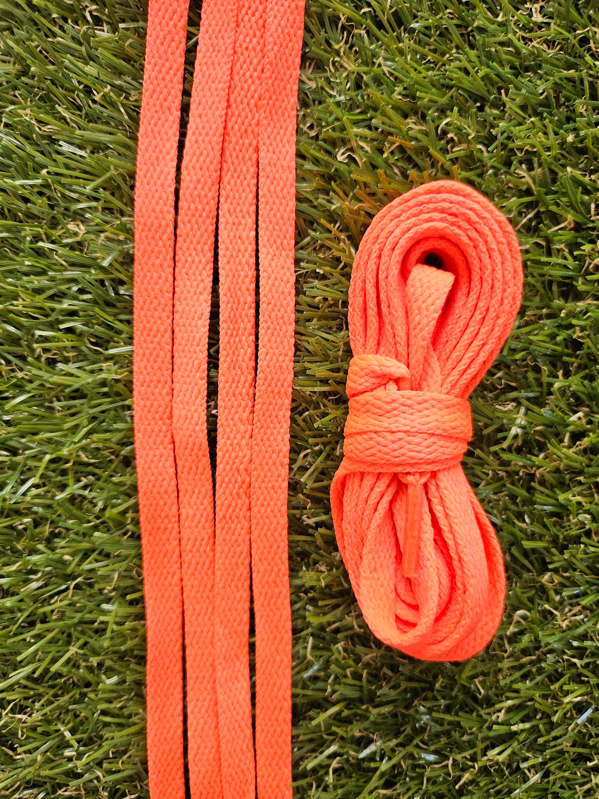Coral orange coloured shoelaces on green grass