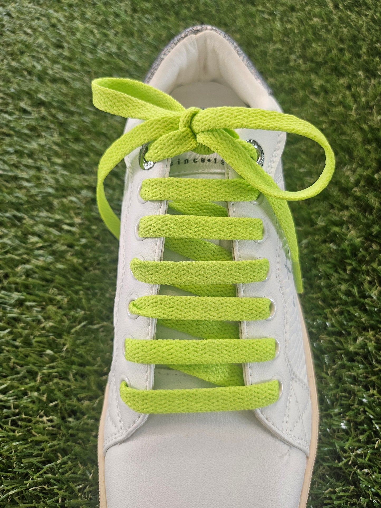 White shoe with bright green shoelaces on a grass background