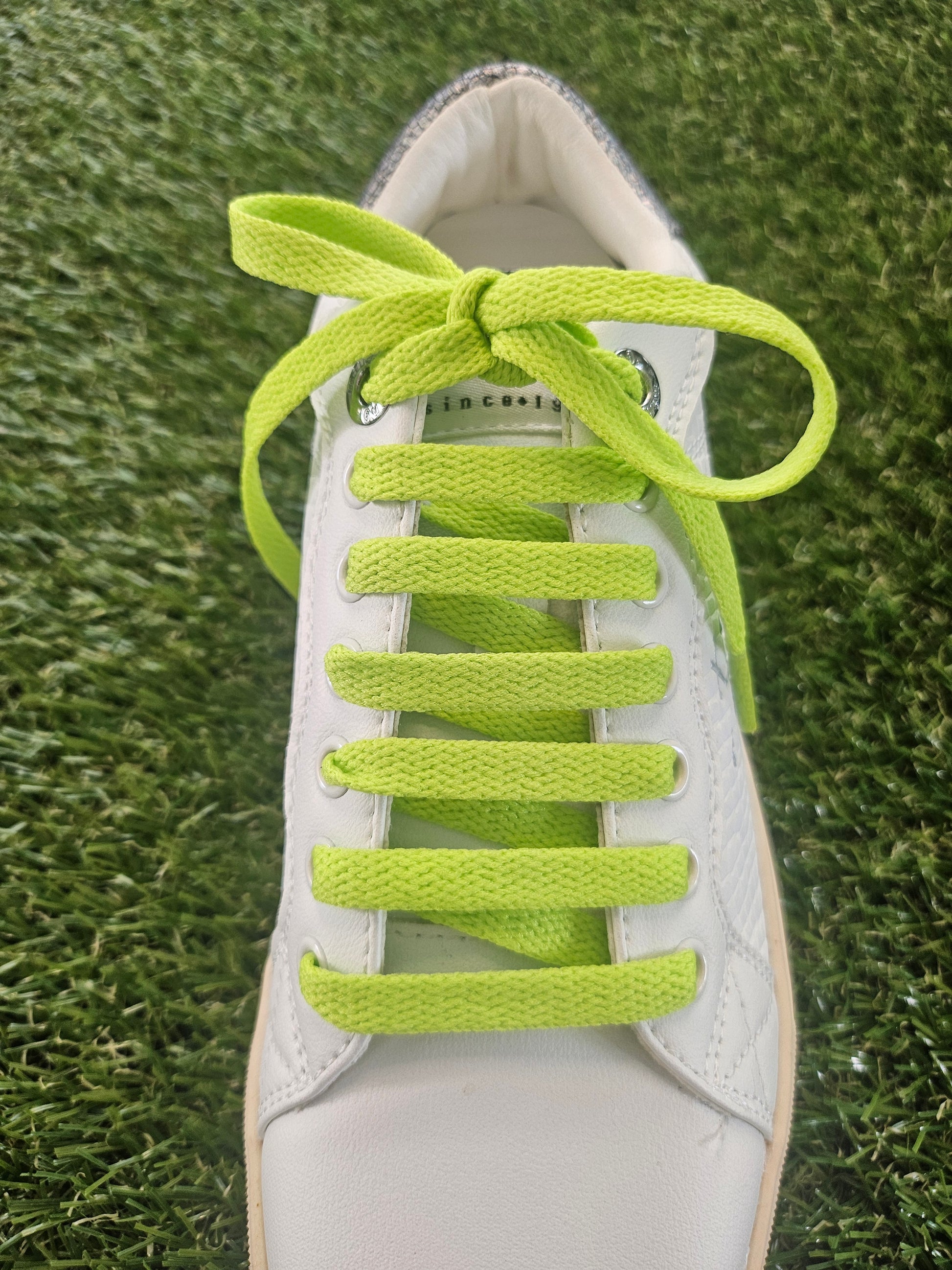 White shoe with bright green shoelaces on a grass background