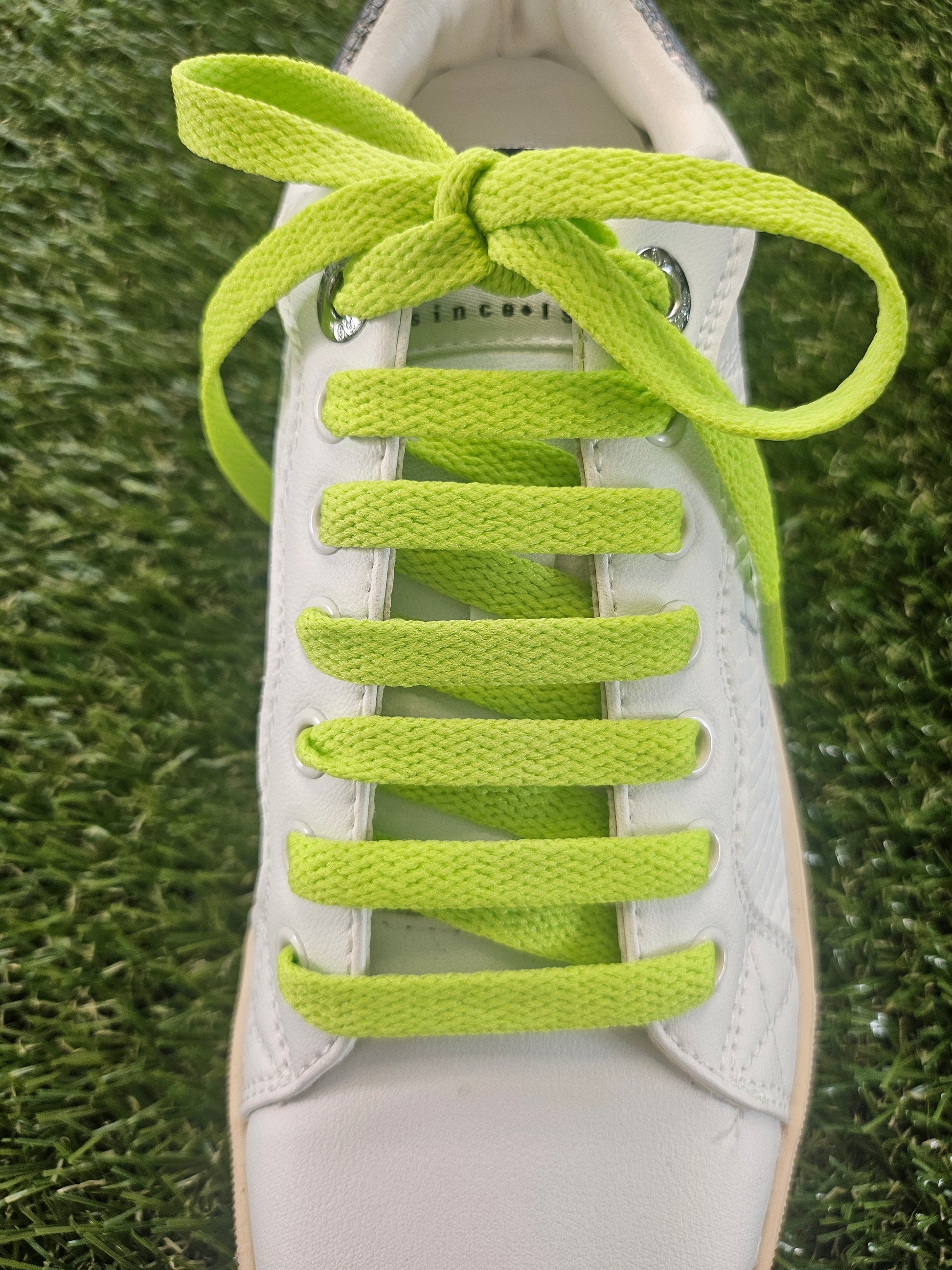 White sneaker with bright green shoelaces on a grass background
