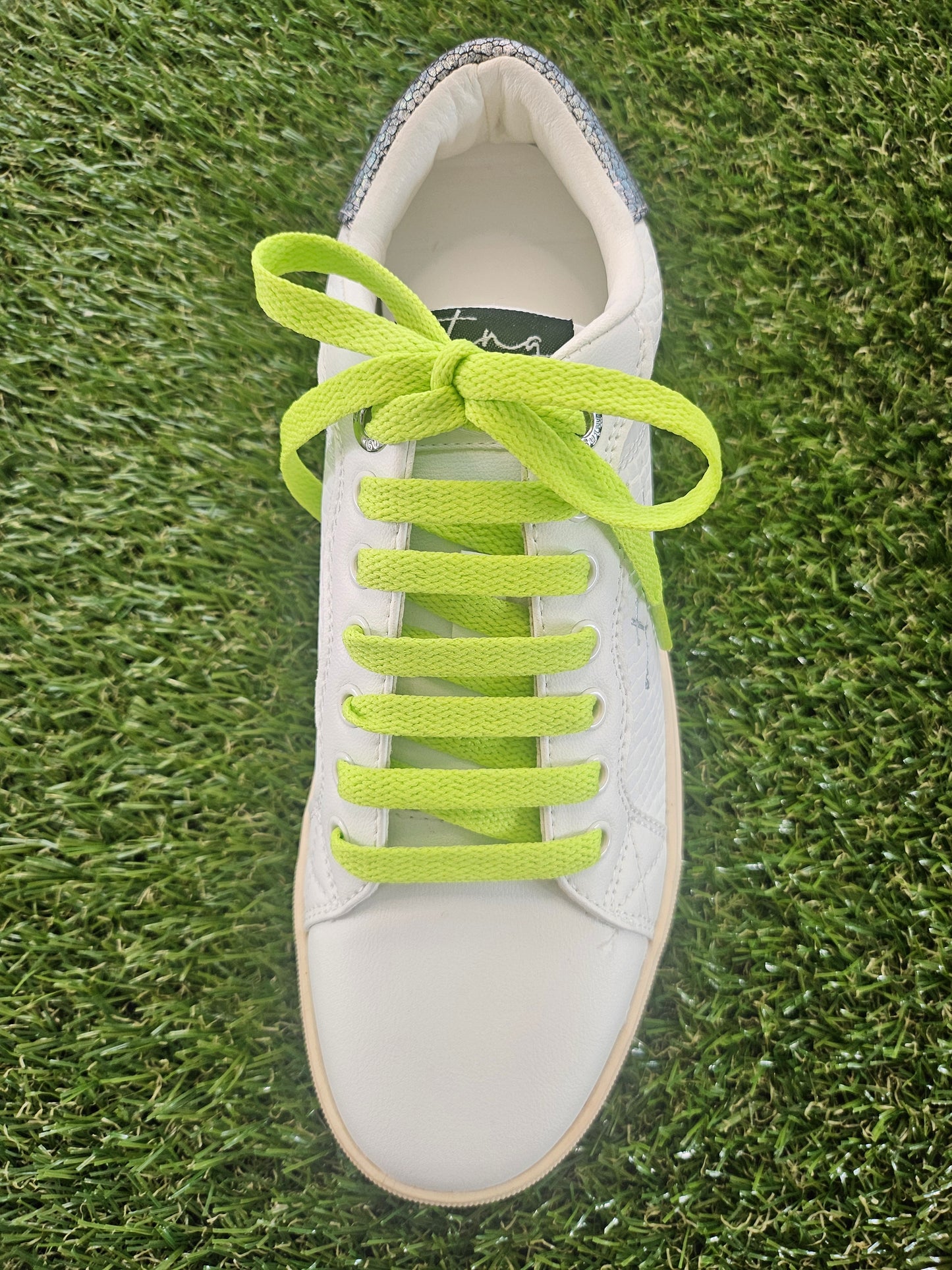 White sneaker with bright green laces on grass