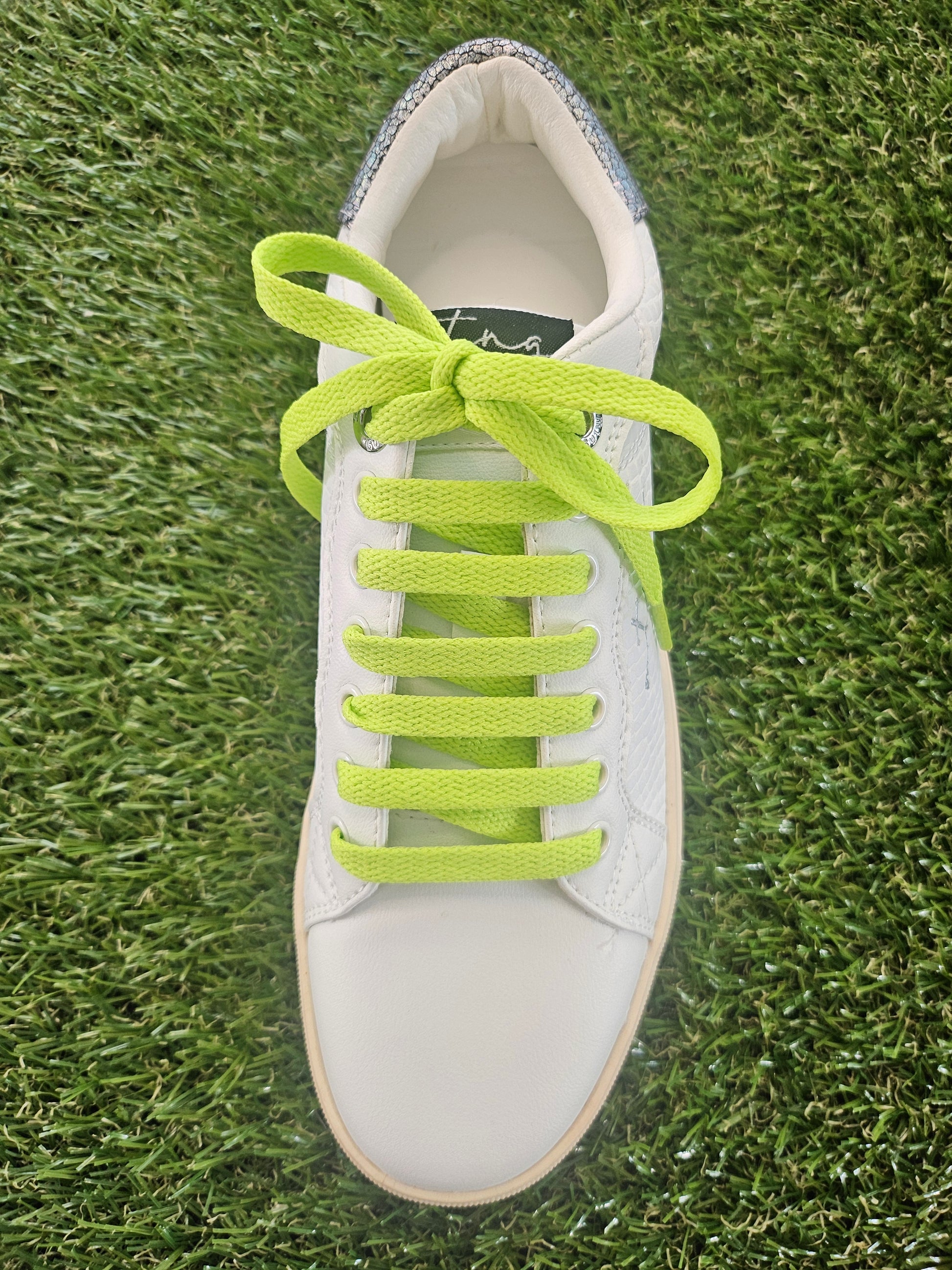 White sneaker with bright green laces on grass