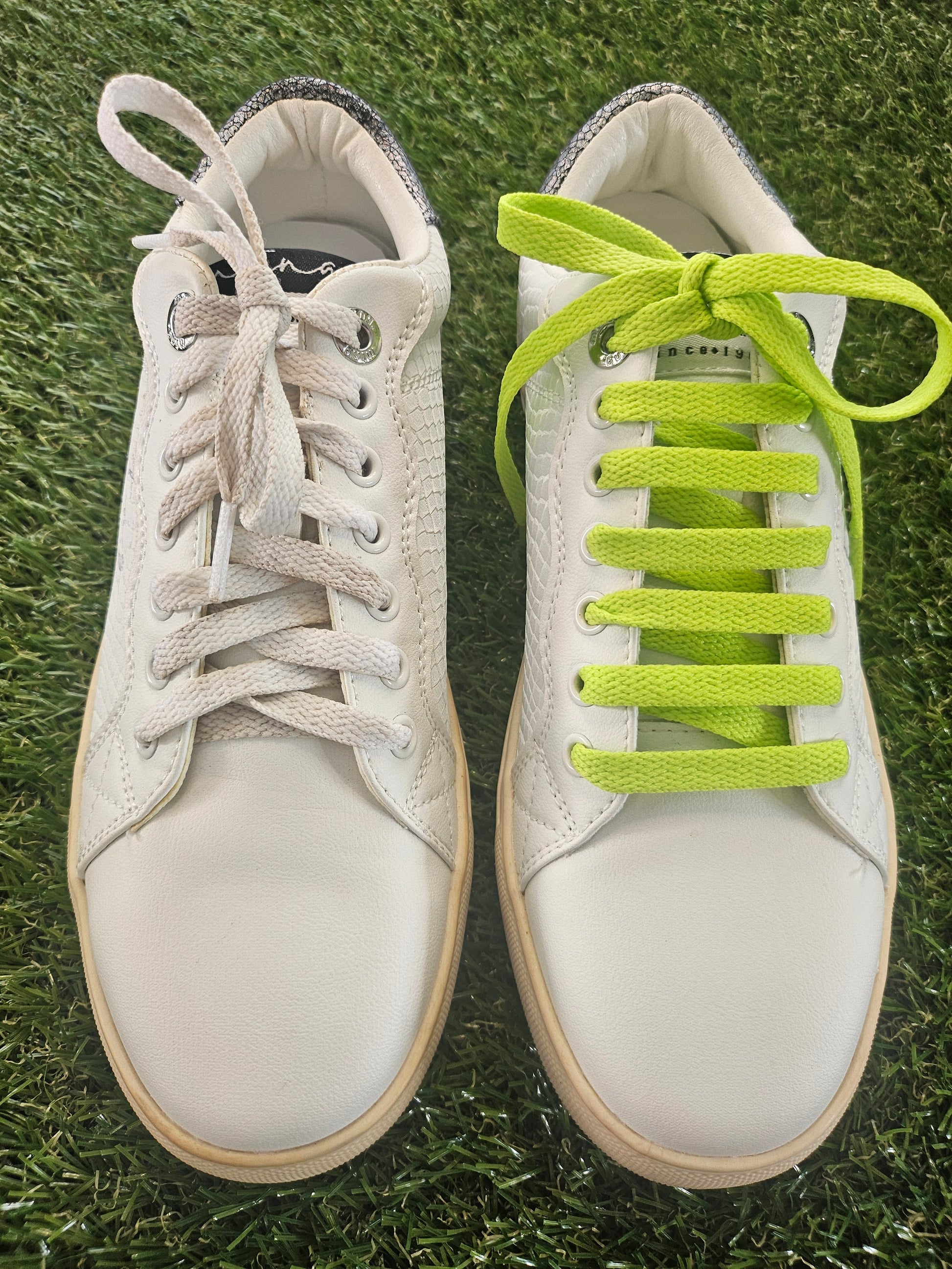 White sneakers with neon green and beige laces on grass