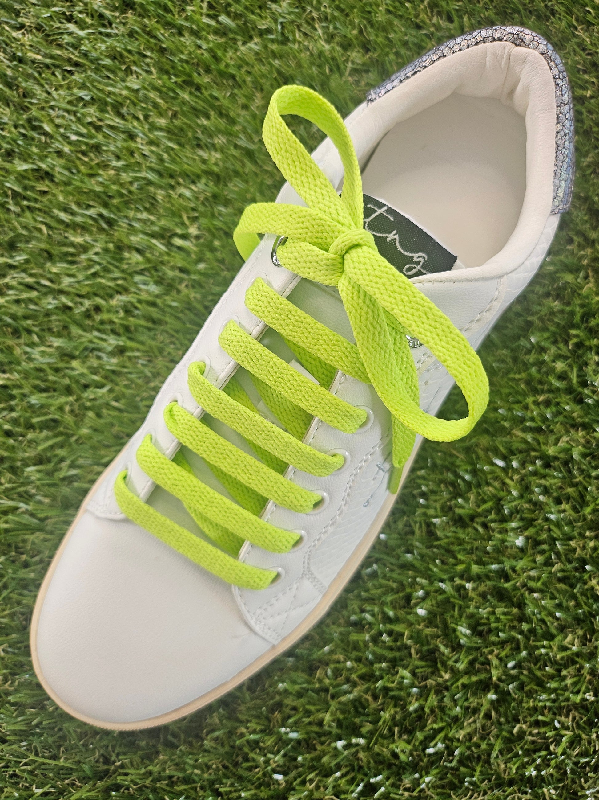 White sneaker with bright green laces on grass