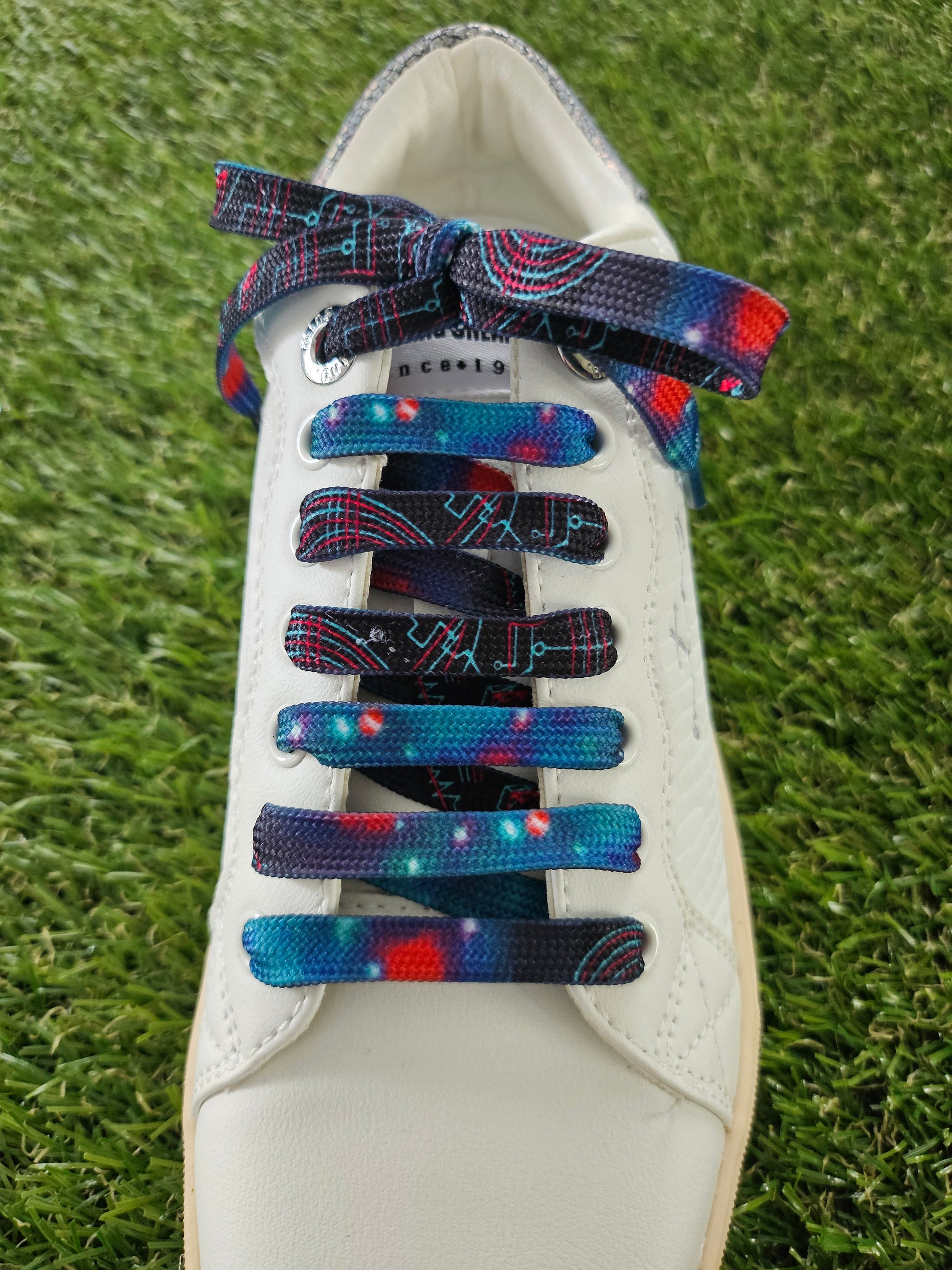 White sneaker with space patterned colorful laces on a grass background