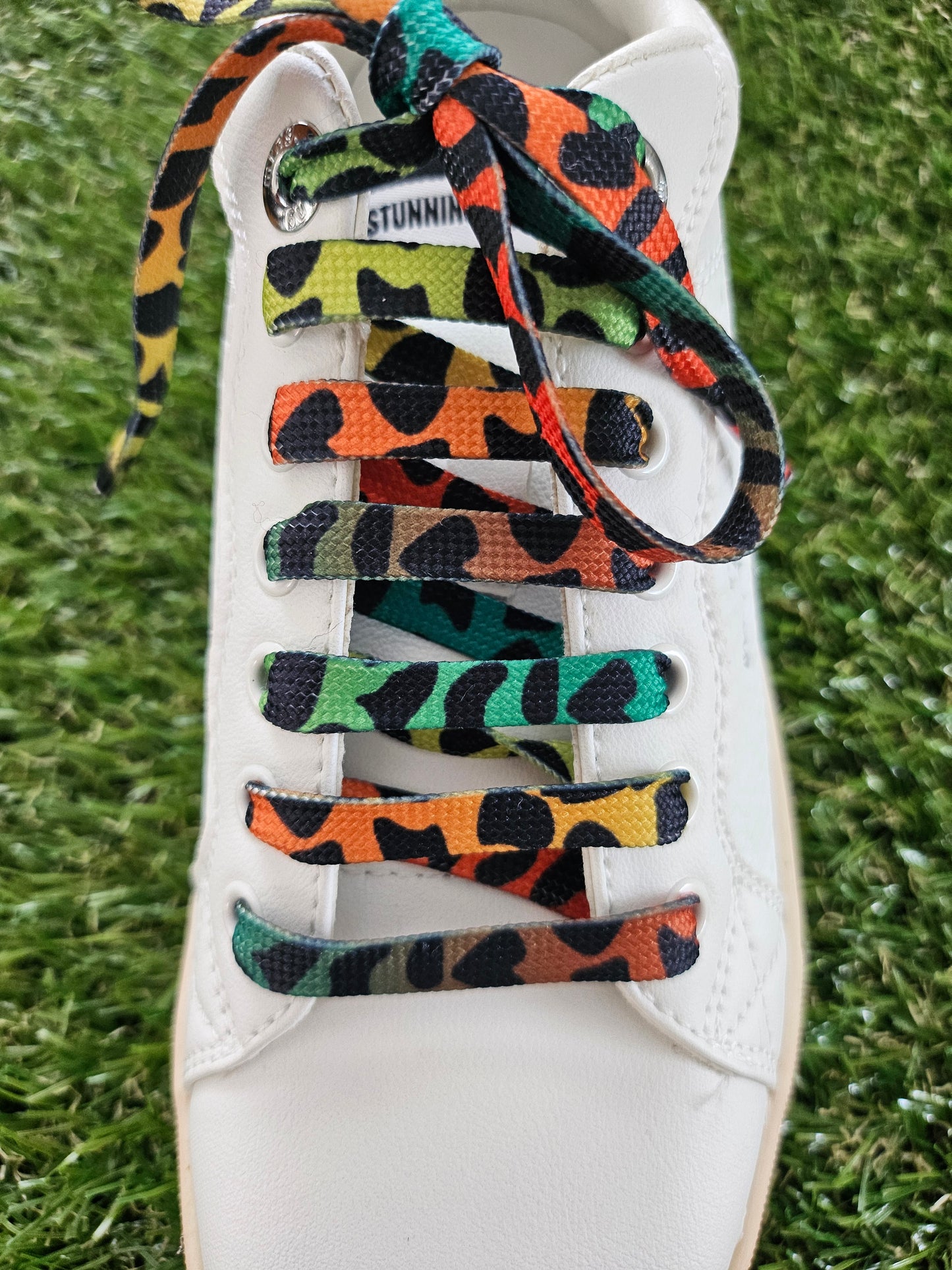 Colorful patterned shoelaces on a white sneaker against a grass background