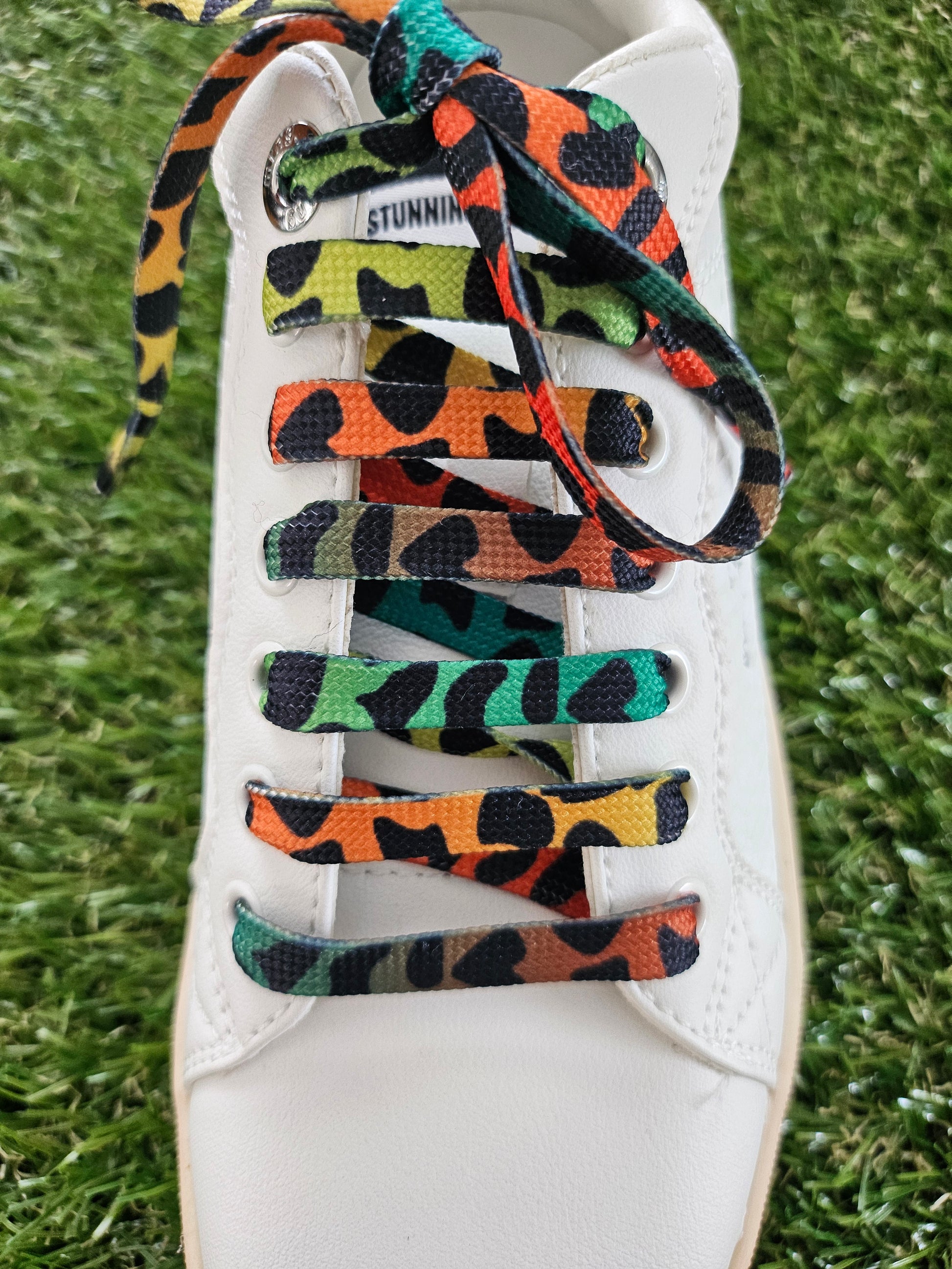 Colorful patterned shoelaces on a white sneaker against a grass background