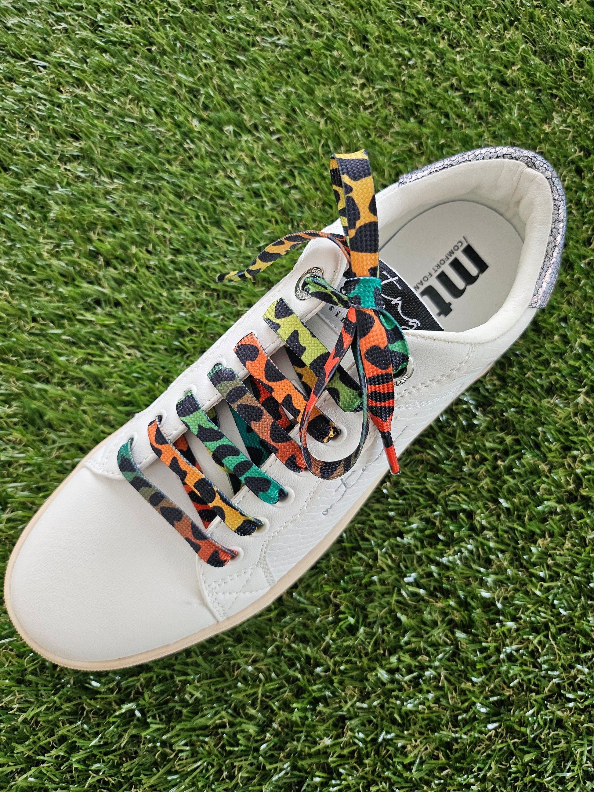 White sneaker with colorful shoelaces on a grass background
