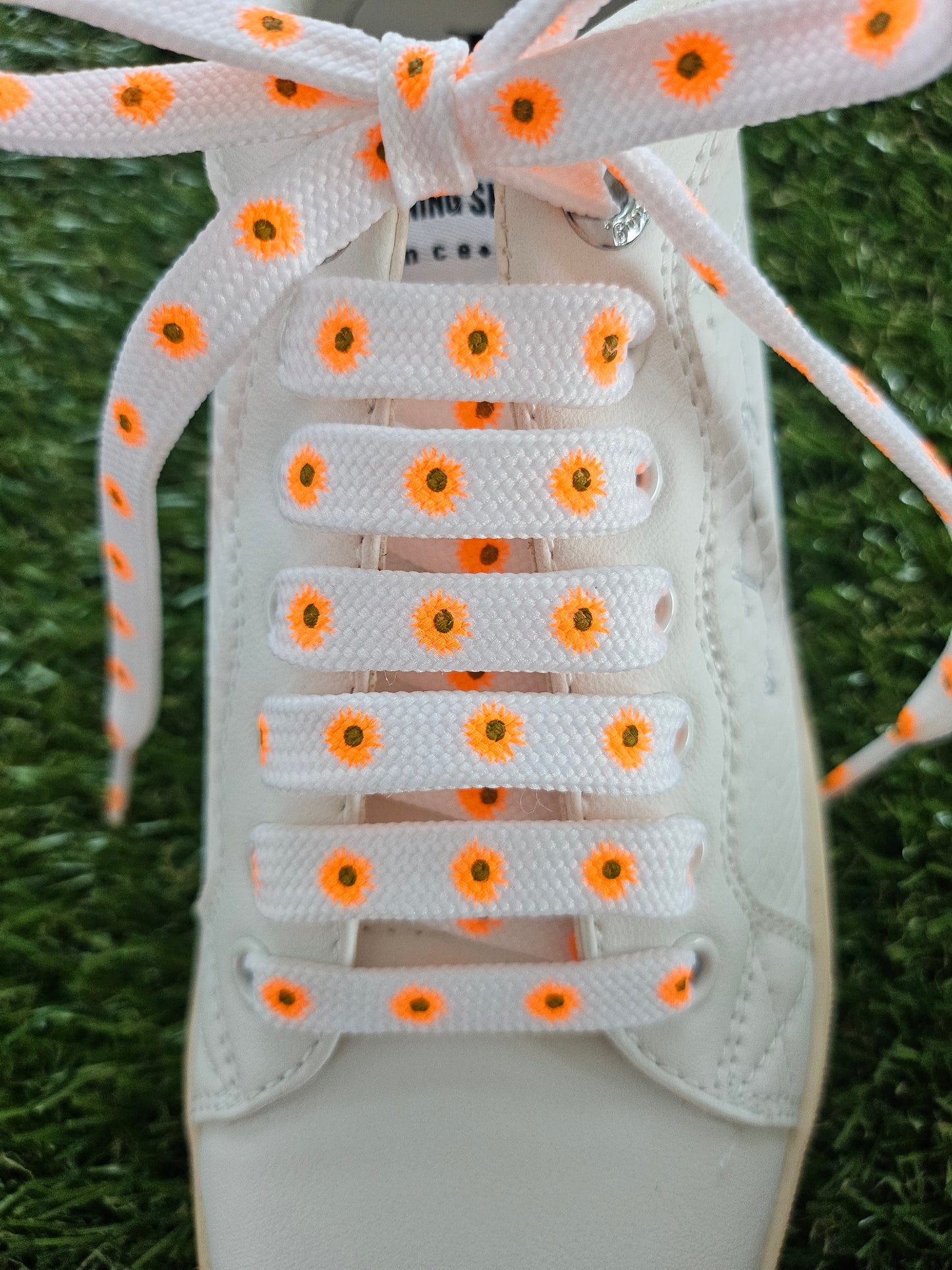 Orange daisies on white shoelaces in white trainers on green grass