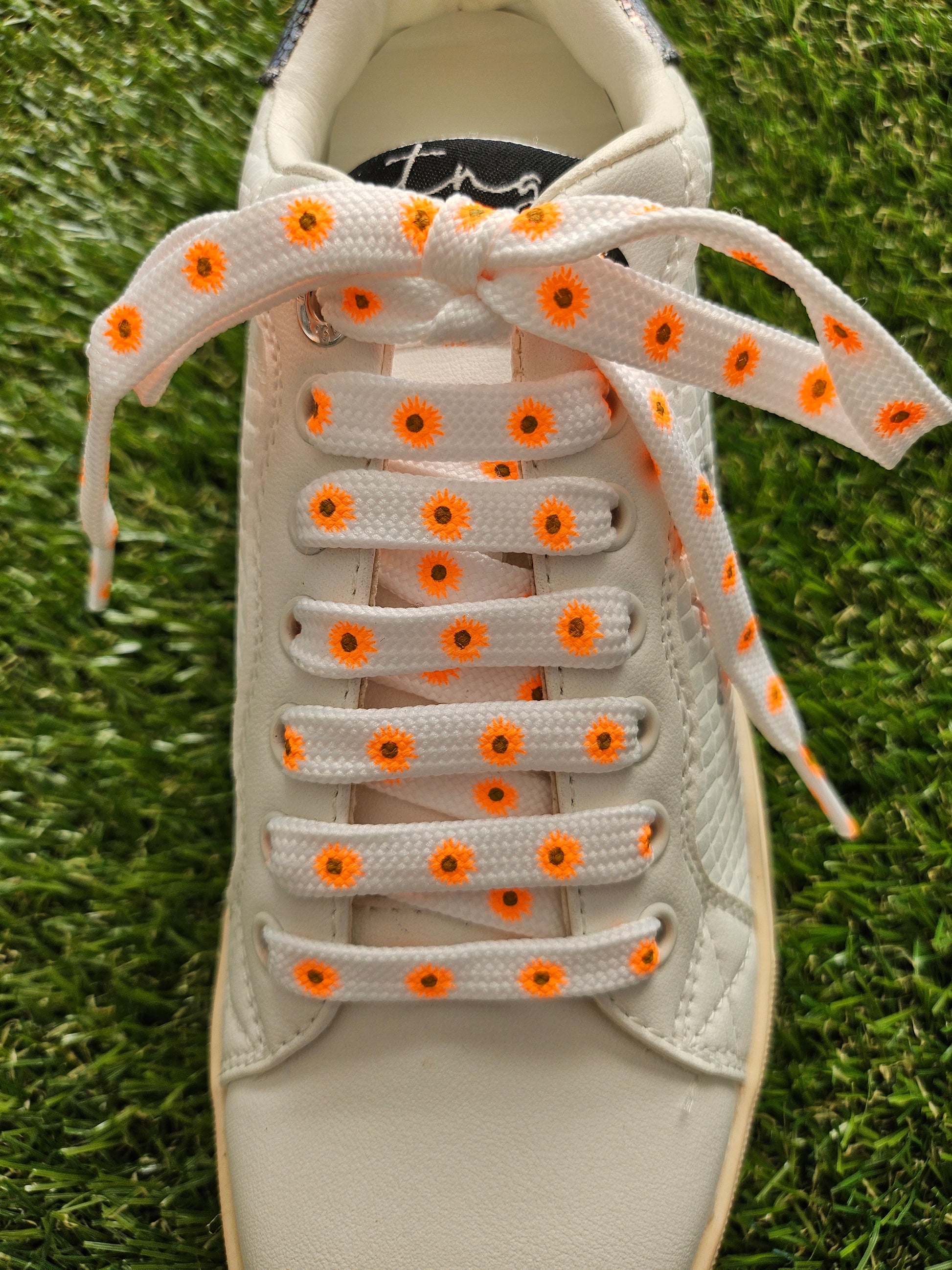 White sneaker with orange daisy laces on a grass background