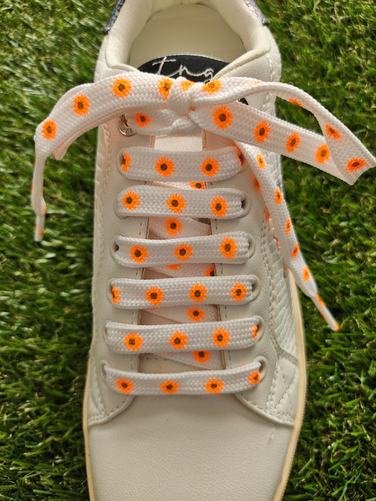 White sneaker with orange daisy laces on a grass background