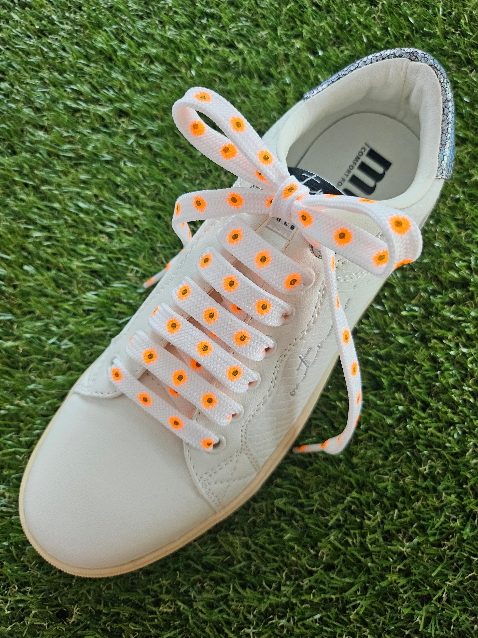 White trainer with orange flower shoelaces on a grass background 