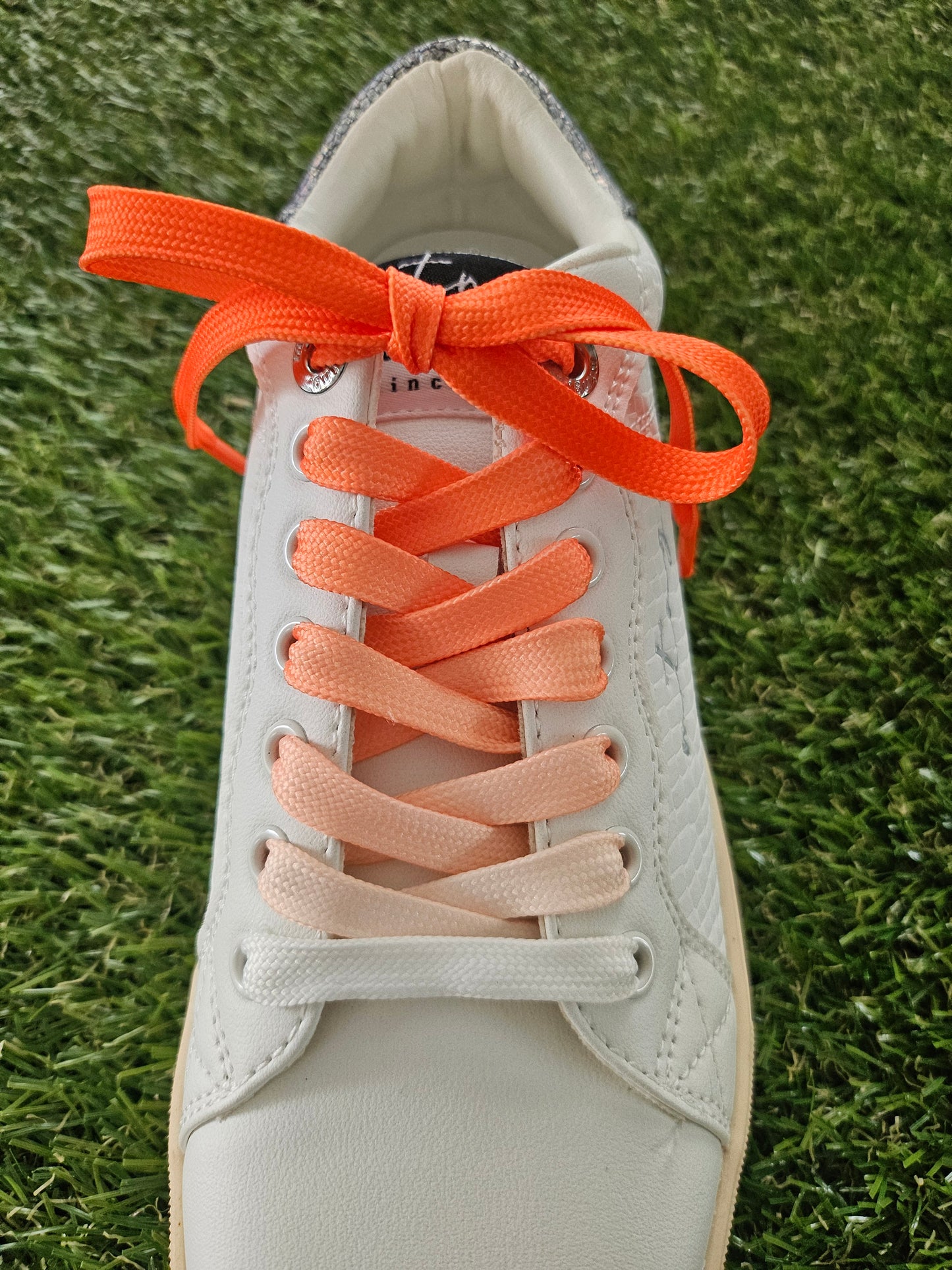 Close-up of a shoe with orange shoelaces on grass