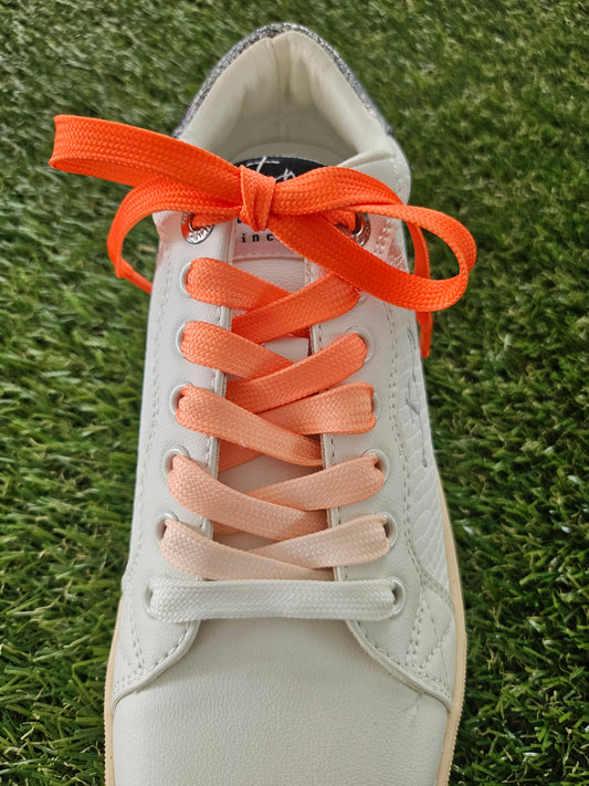Close-up of a shoe with orange shoelaces on grass