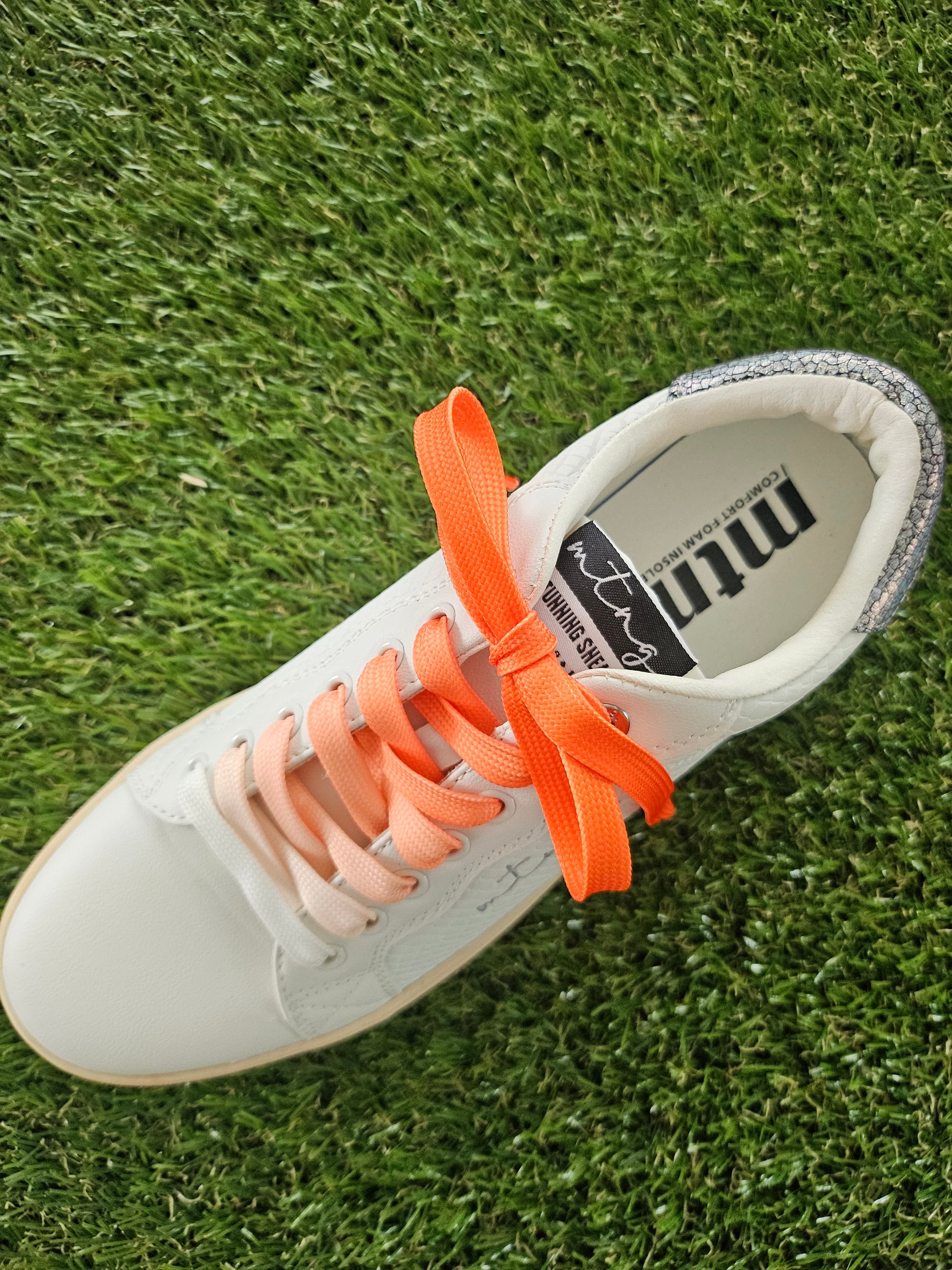 White sneaker with colorful shoelaces on a grass background