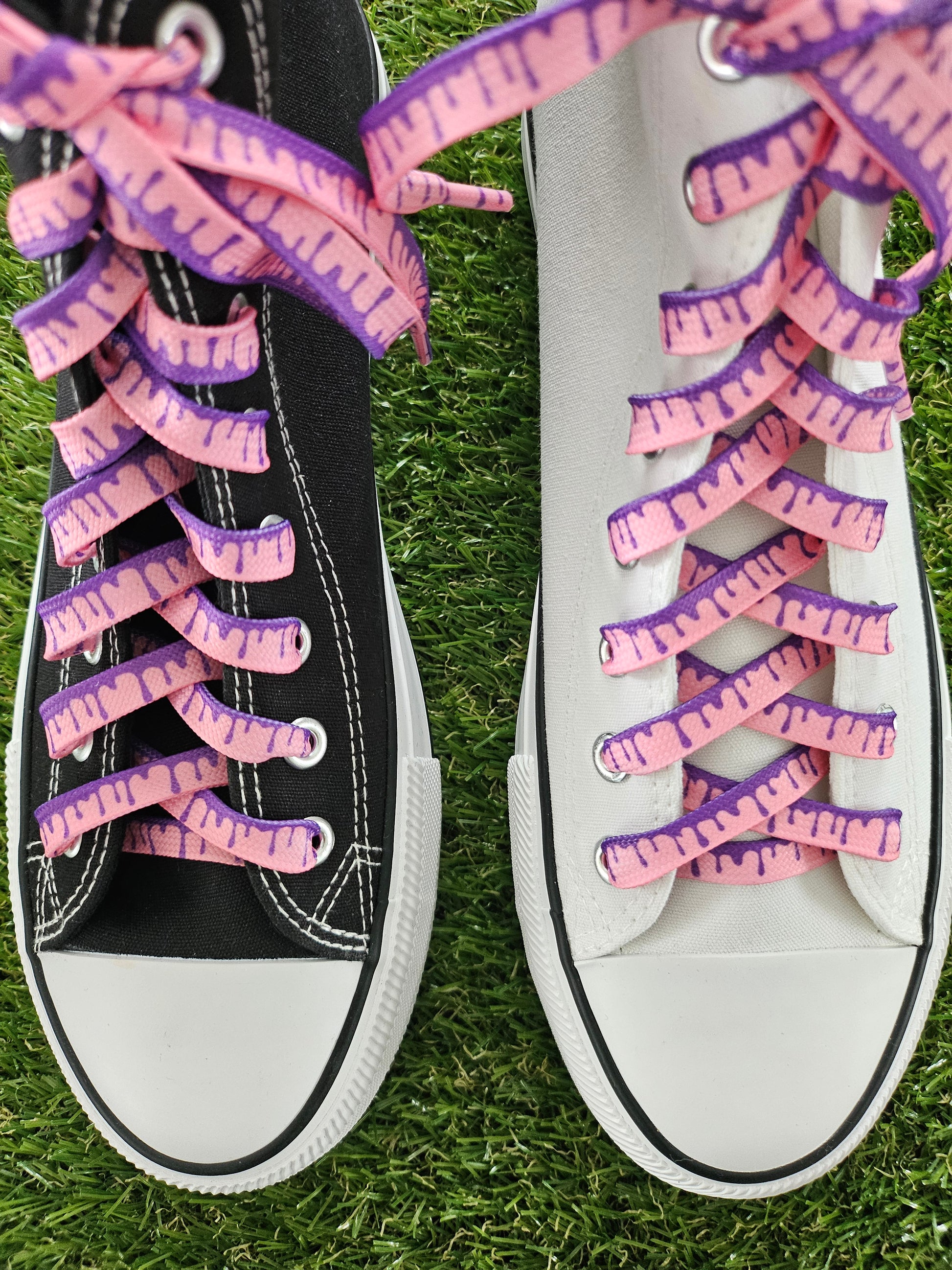 White and black sneakers with unique pink and purple shoelaces on grass.