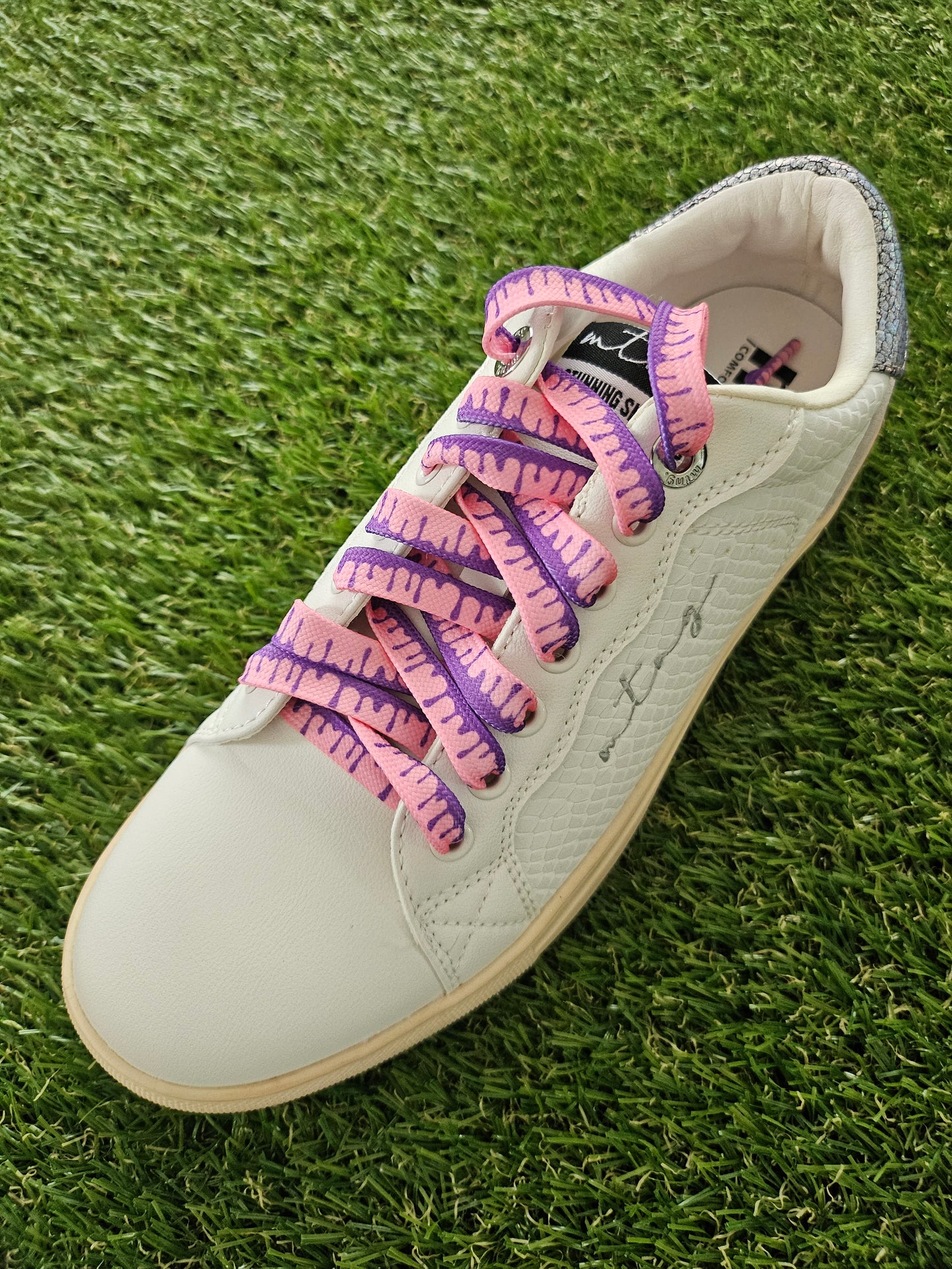 White sneaker with pink and purple shoelaces on grass