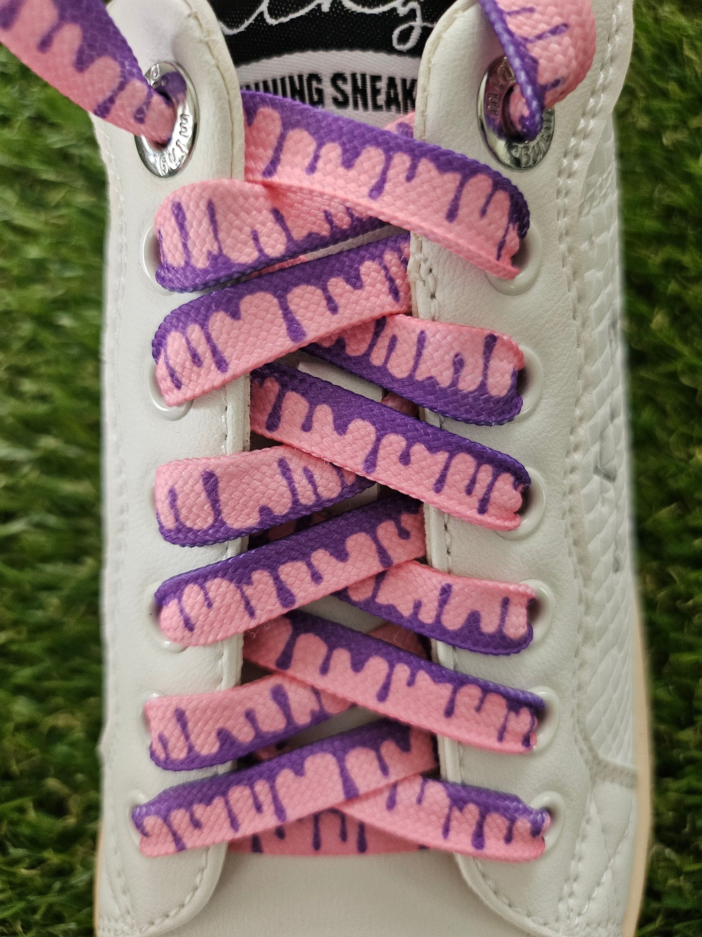 Close-up of a sneaker with pink and purple patterned laces on grass.