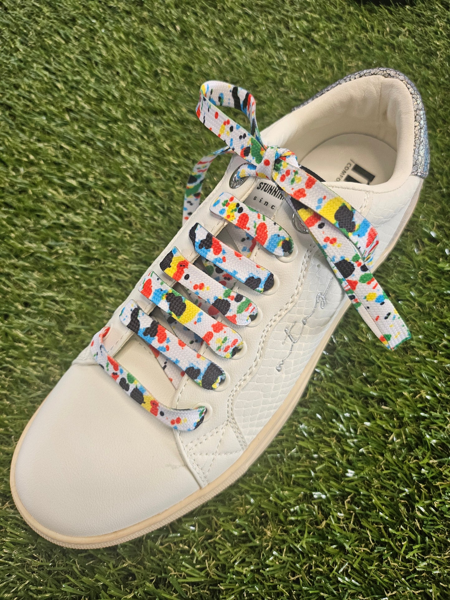 White sneaker with colorful laces on grass