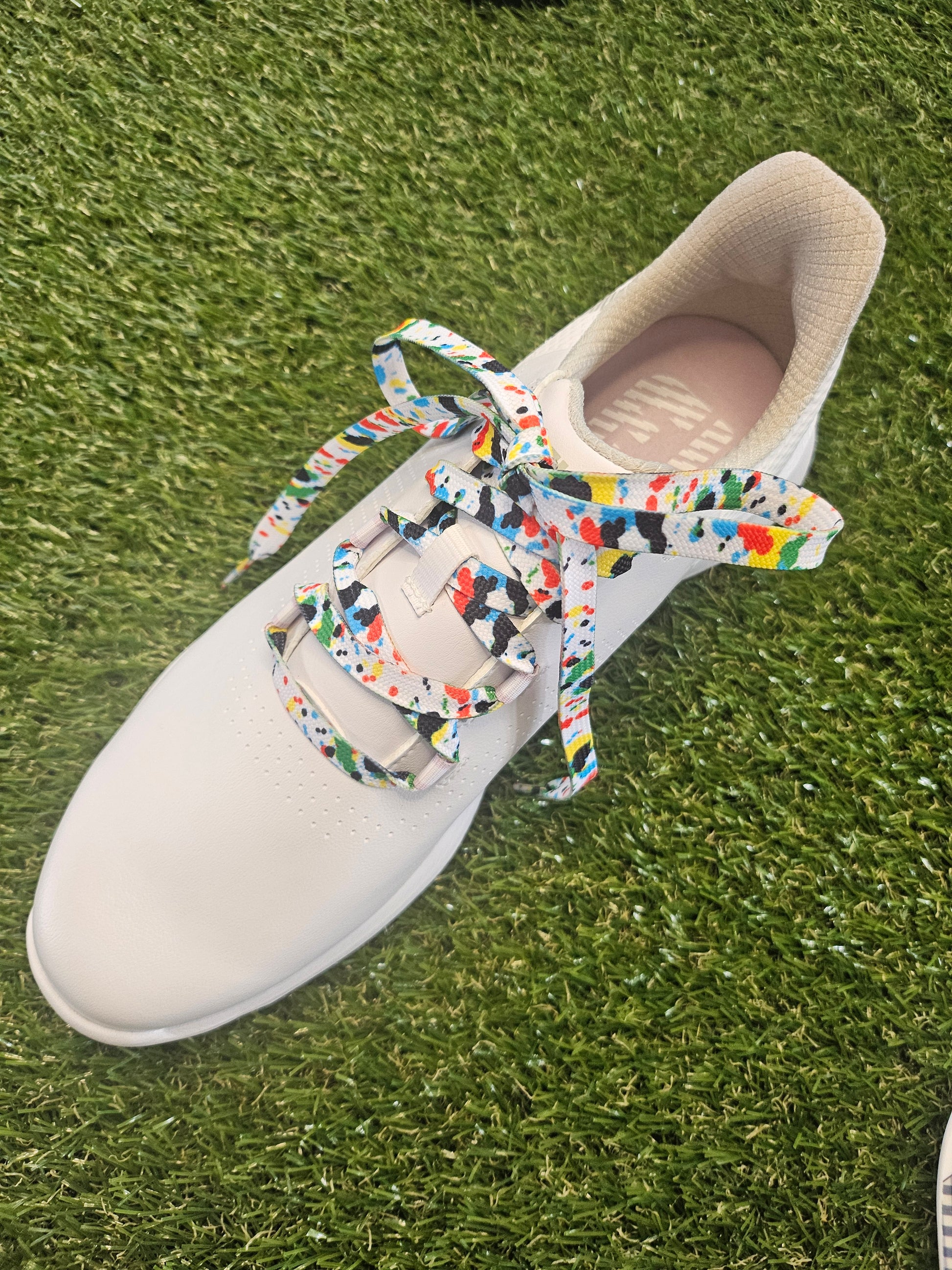 White ladies golf shoe with colourful paint splash laces on grass