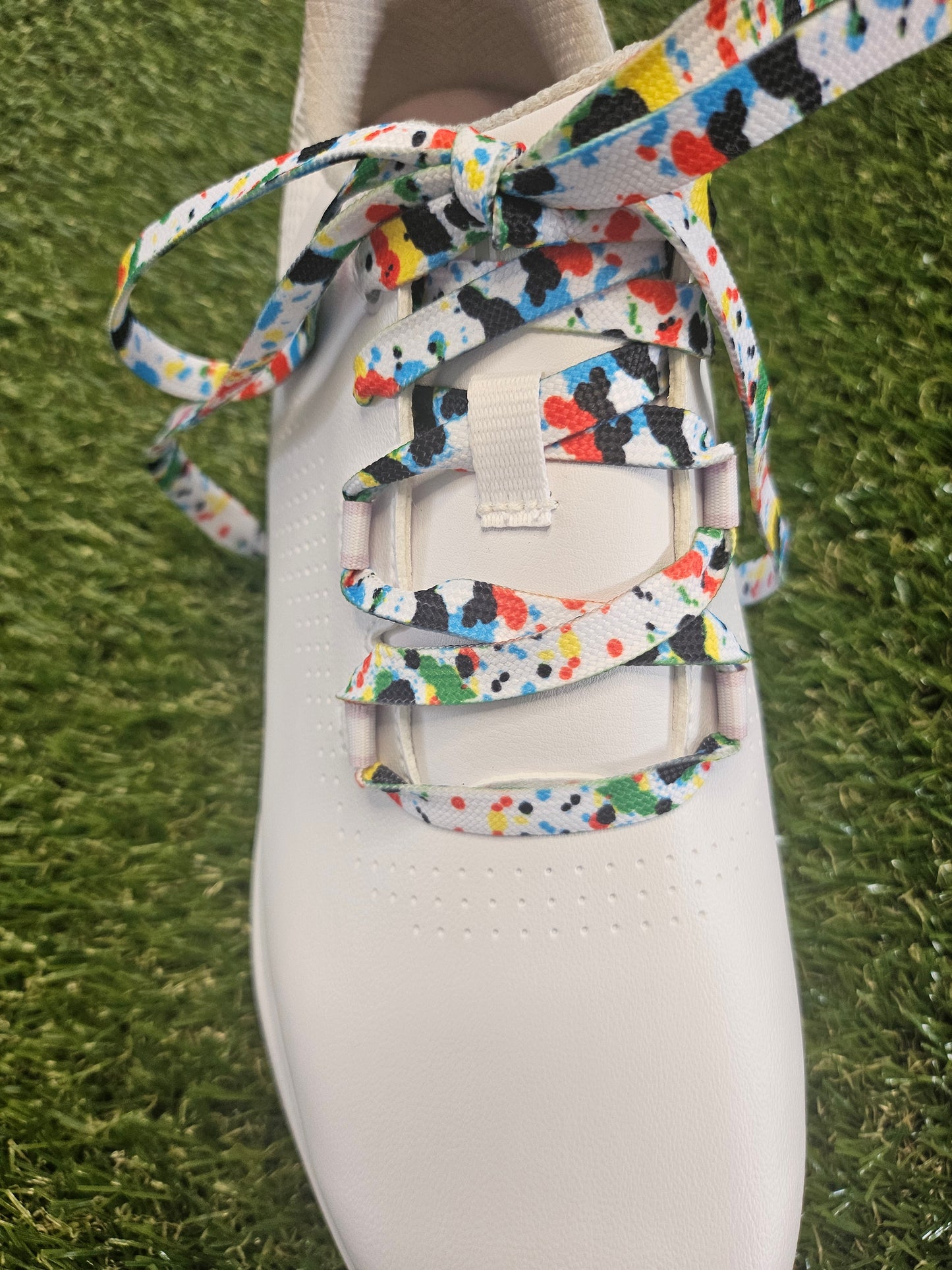 White womans golf shoe with colourful paint splash laces on grass