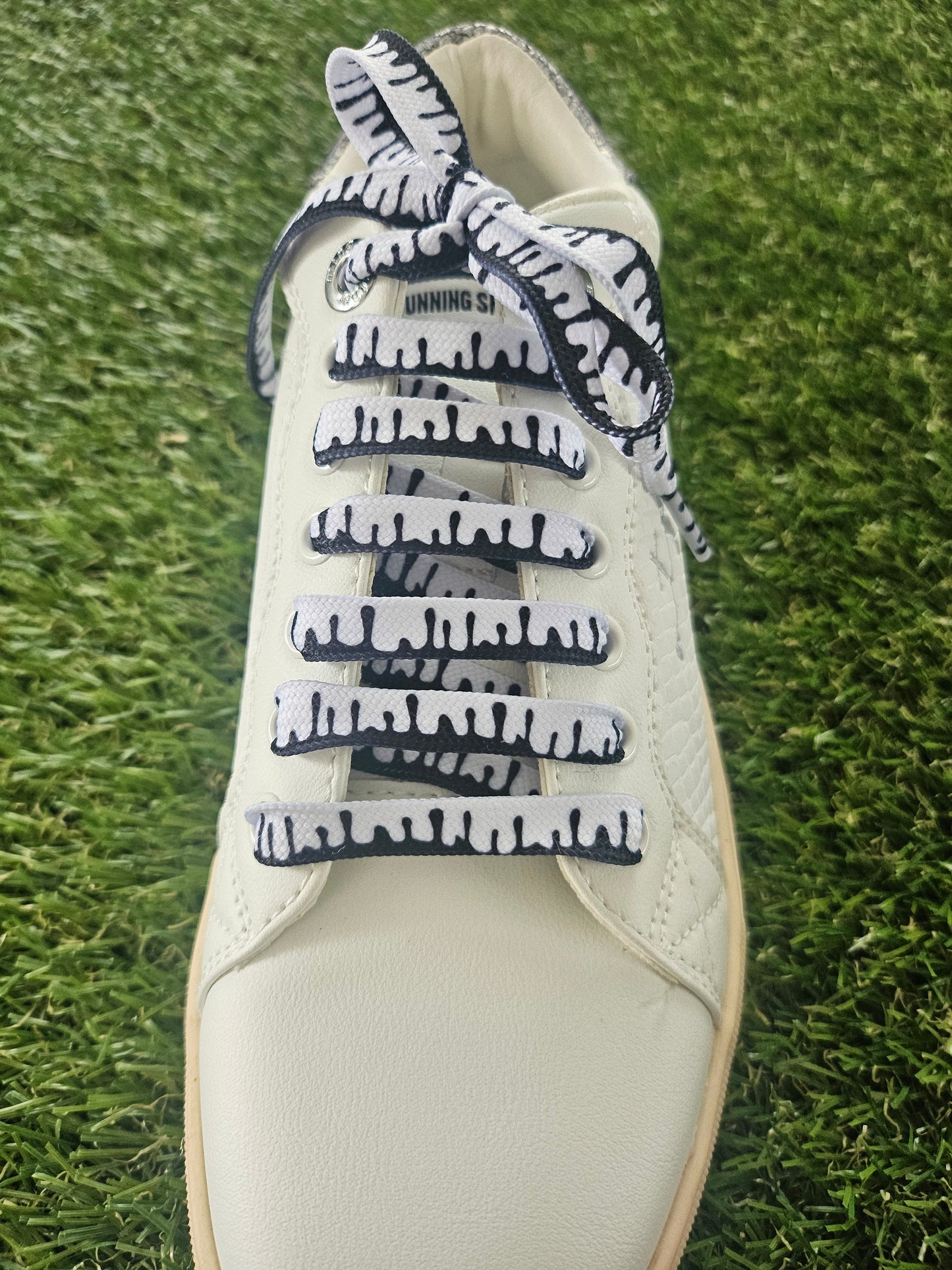 White sneaker with black and white patterned designer shoelaces on grass