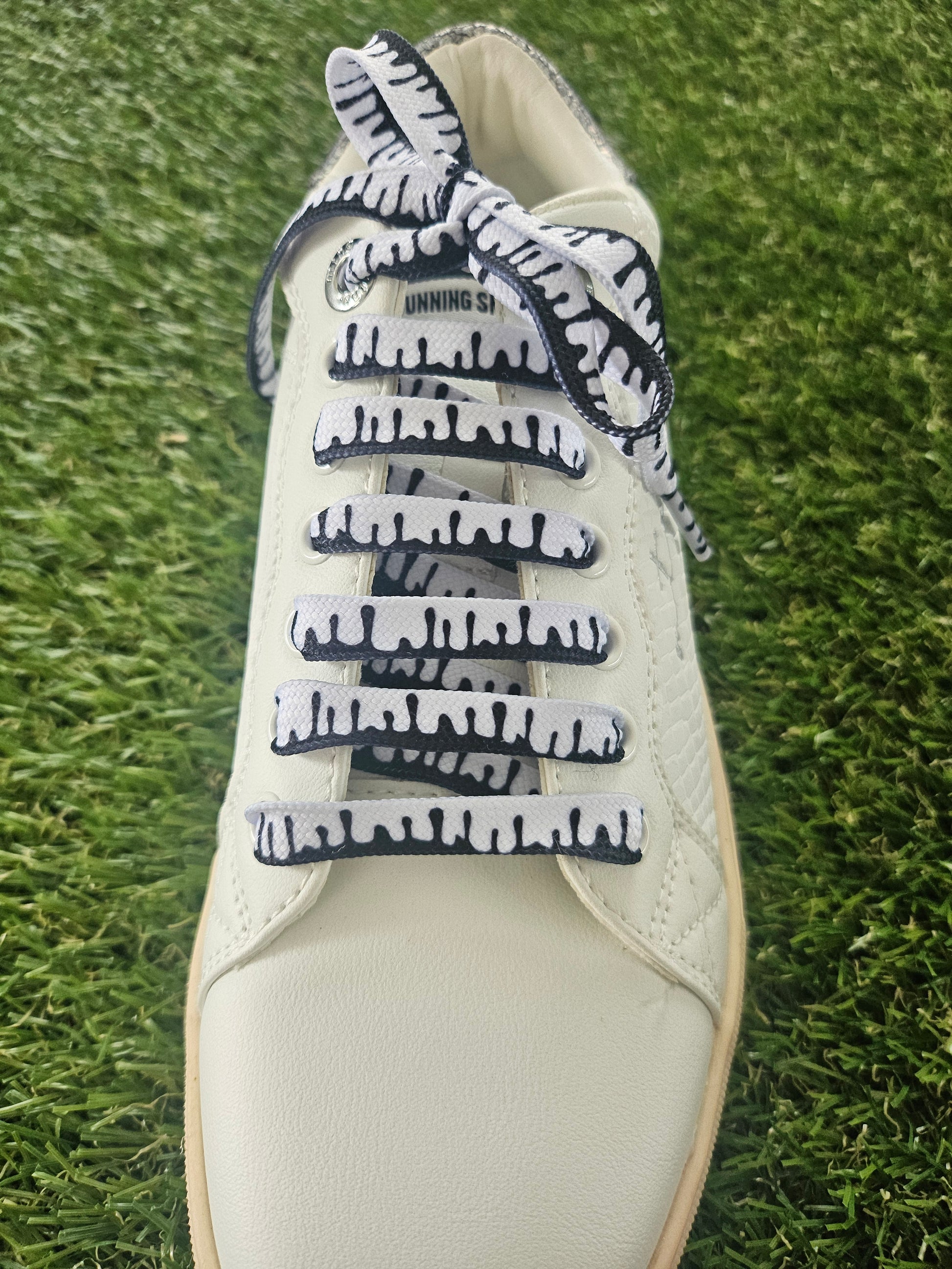 White sneaker with black and white patterned designer shoelaces on grass