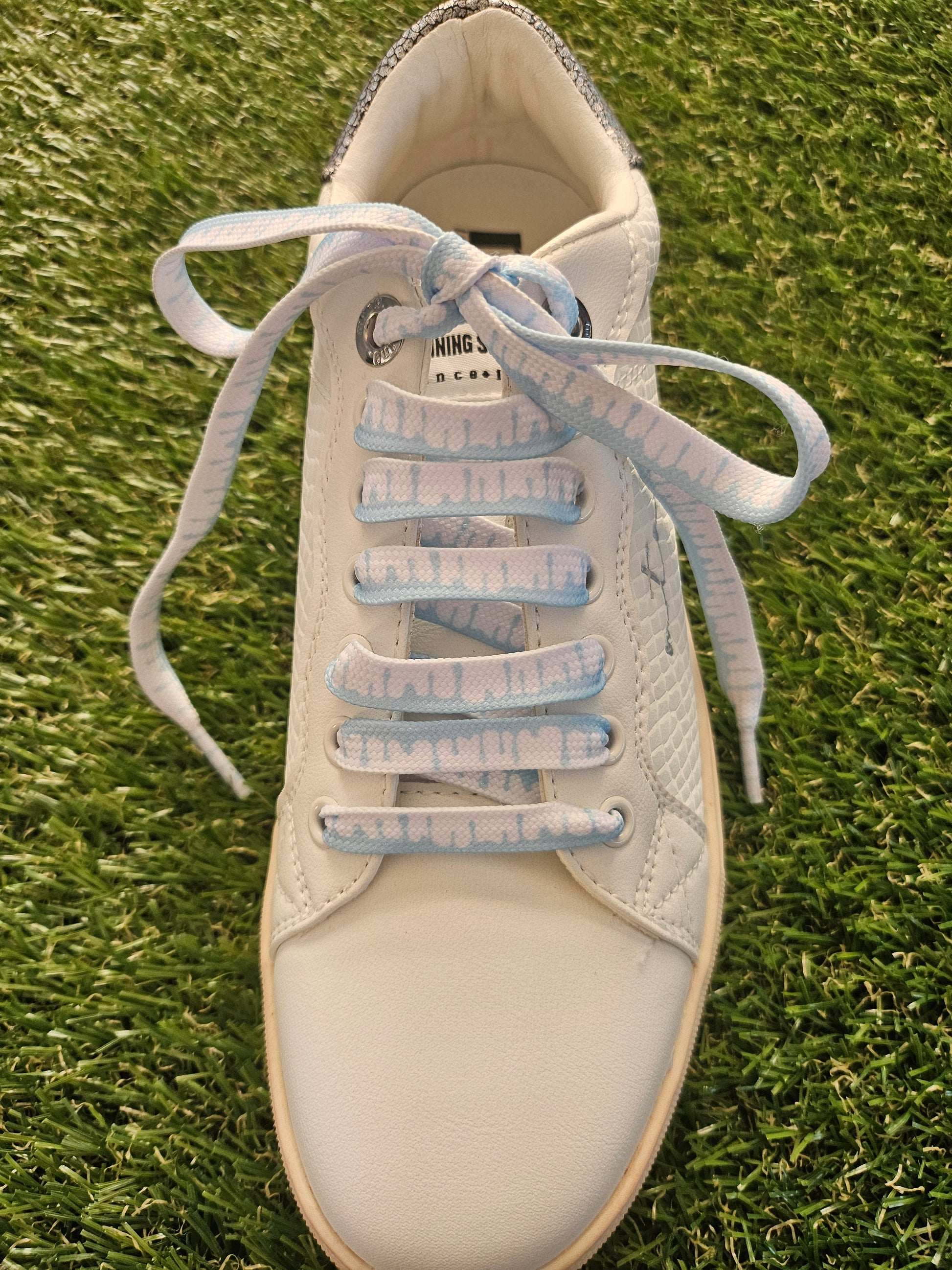 White sneaker with pale blue laces on a grass background