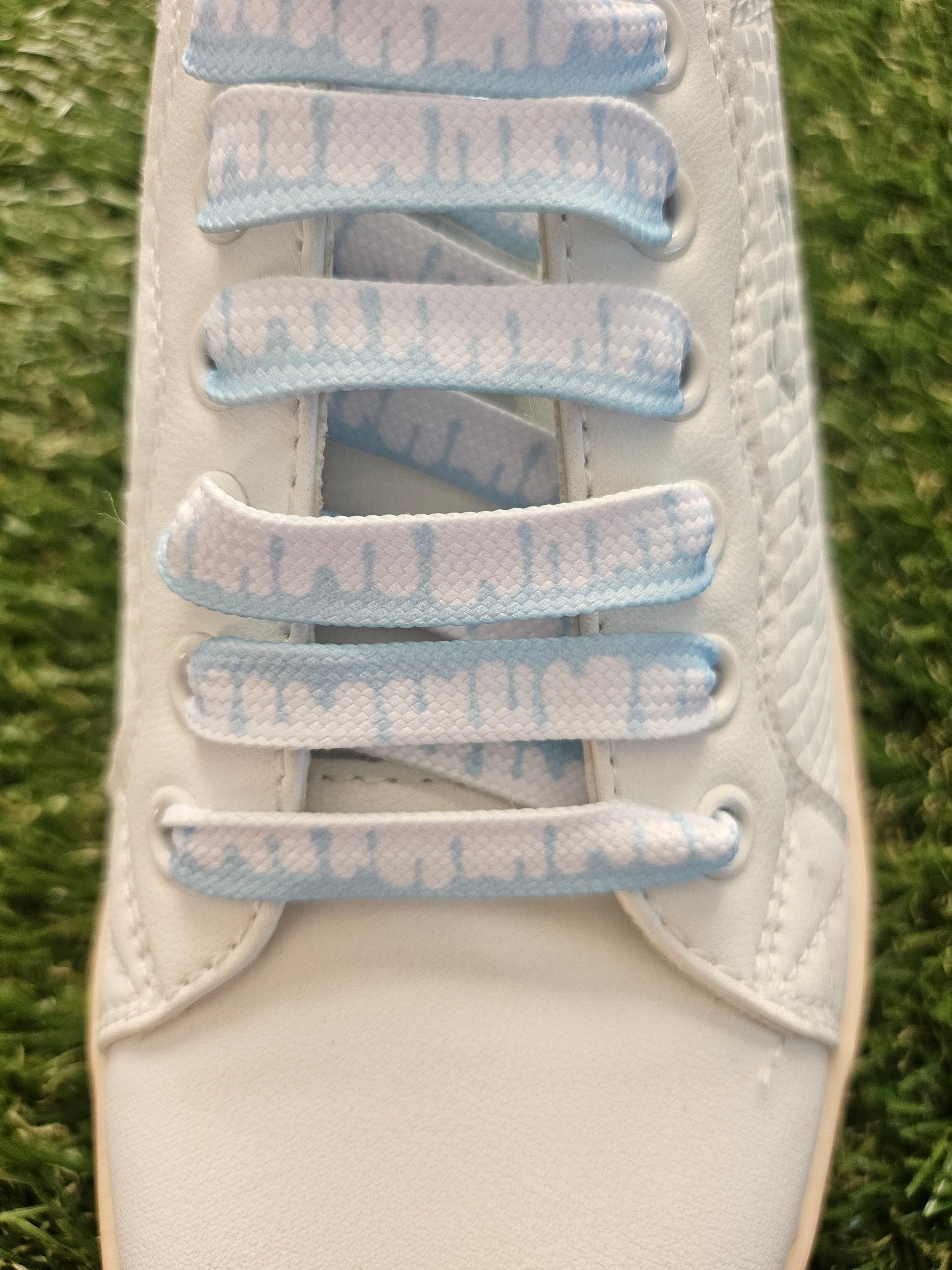 White trainer with blue and white shoelaces on a grass background