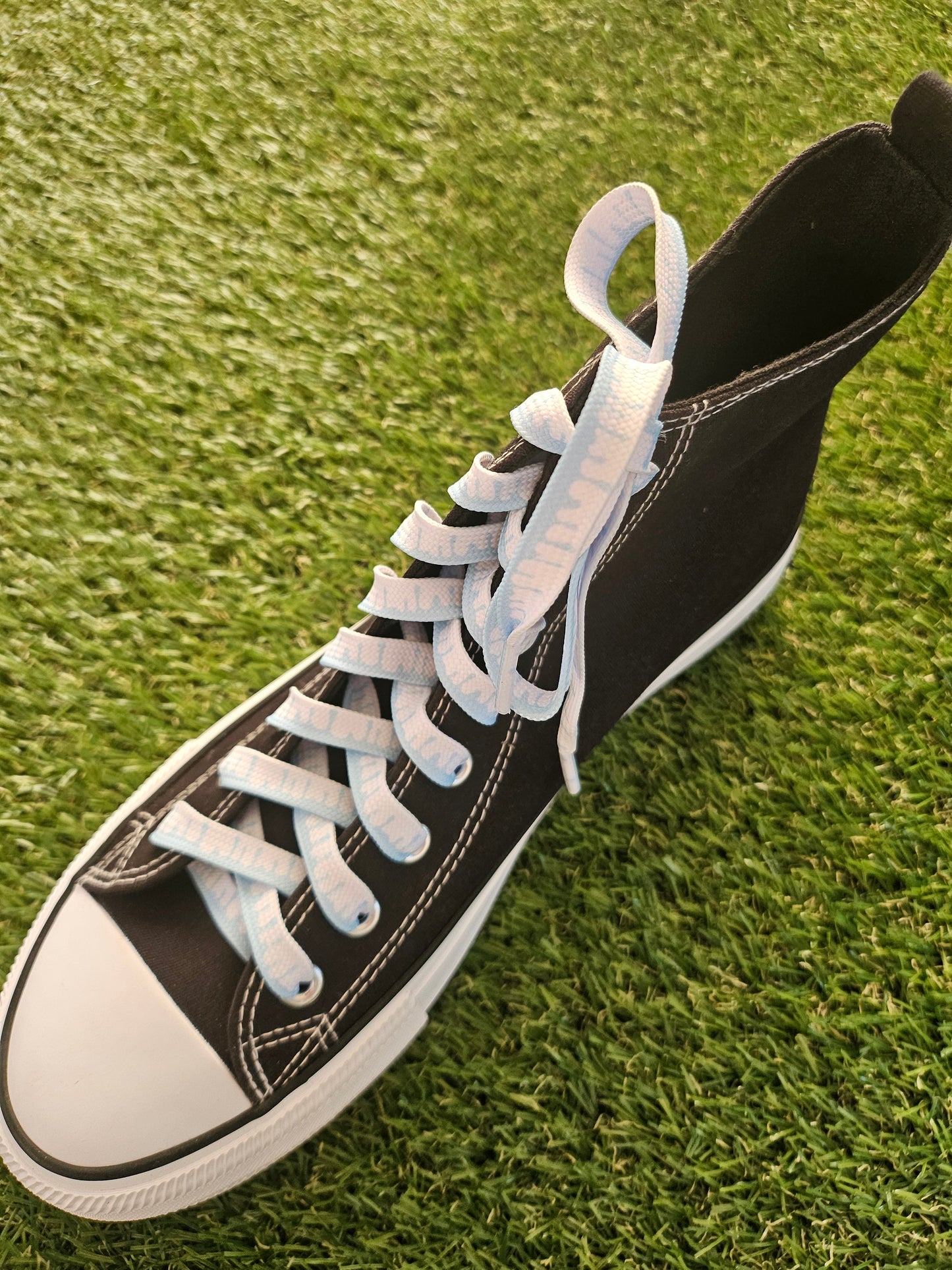 Black high-top sneaker with white laces on grass