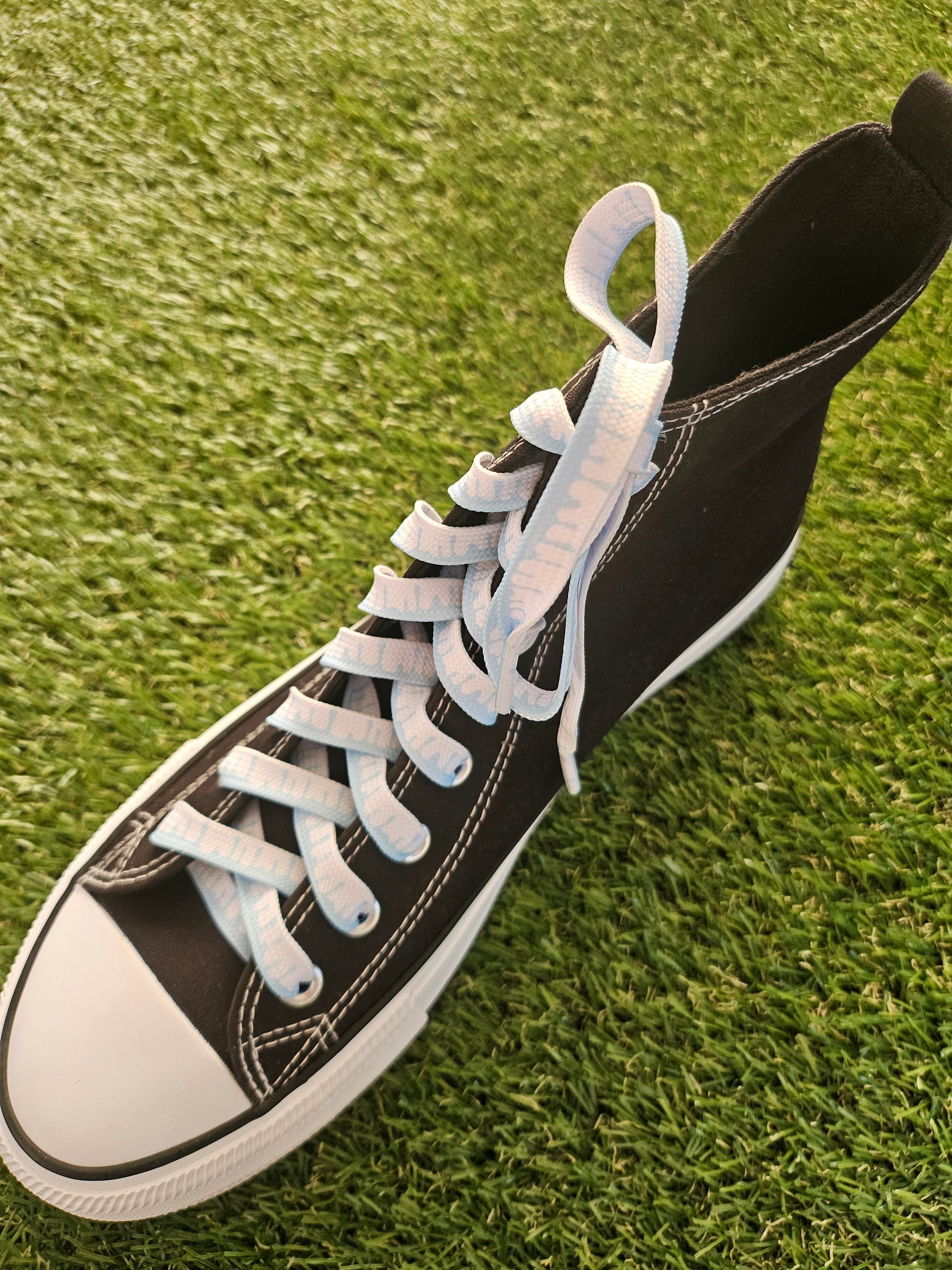 Black high-top sneaker with white laces on grass