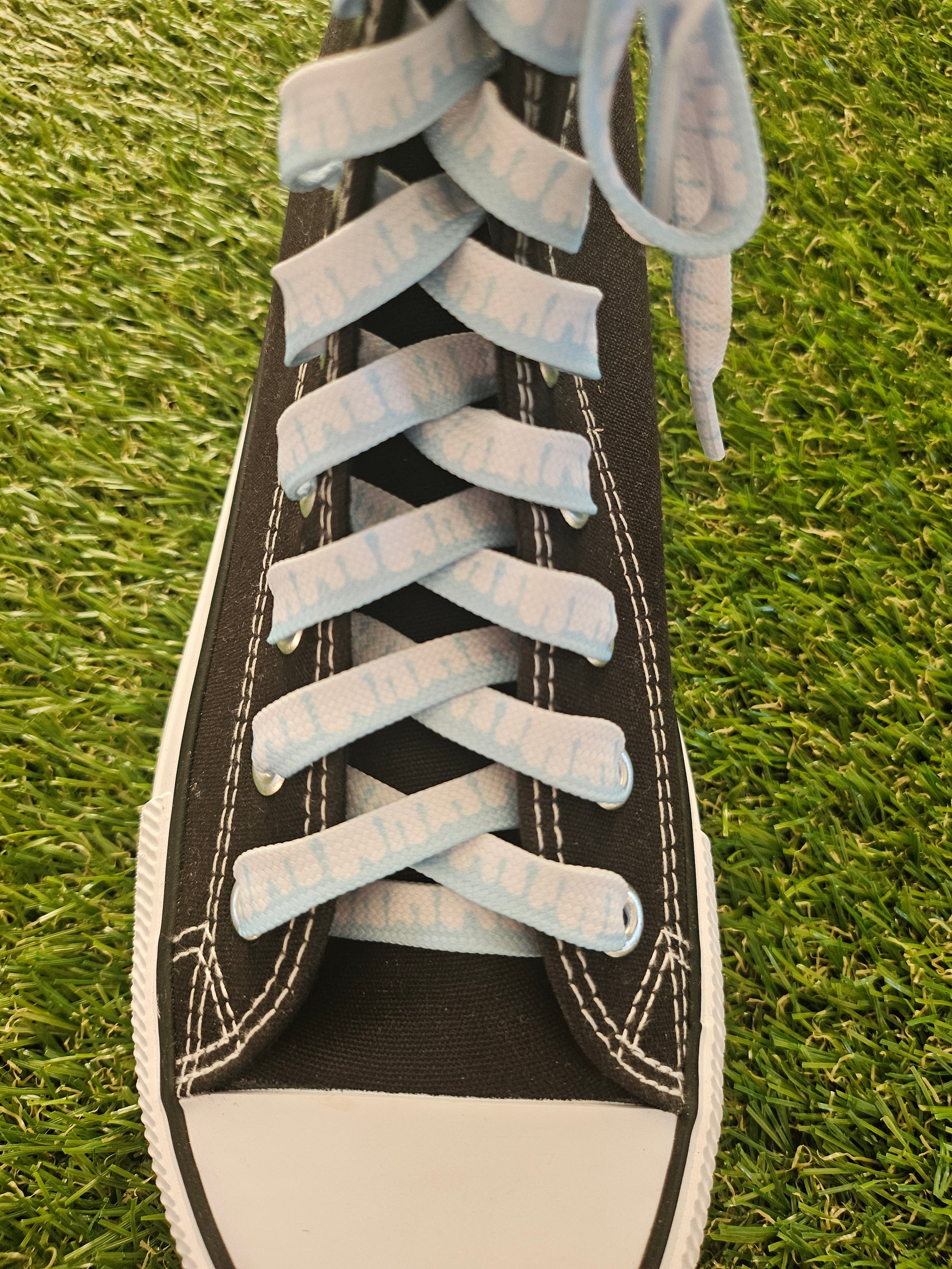 Close-up of a black sneaker with white  and light blue laces on grass