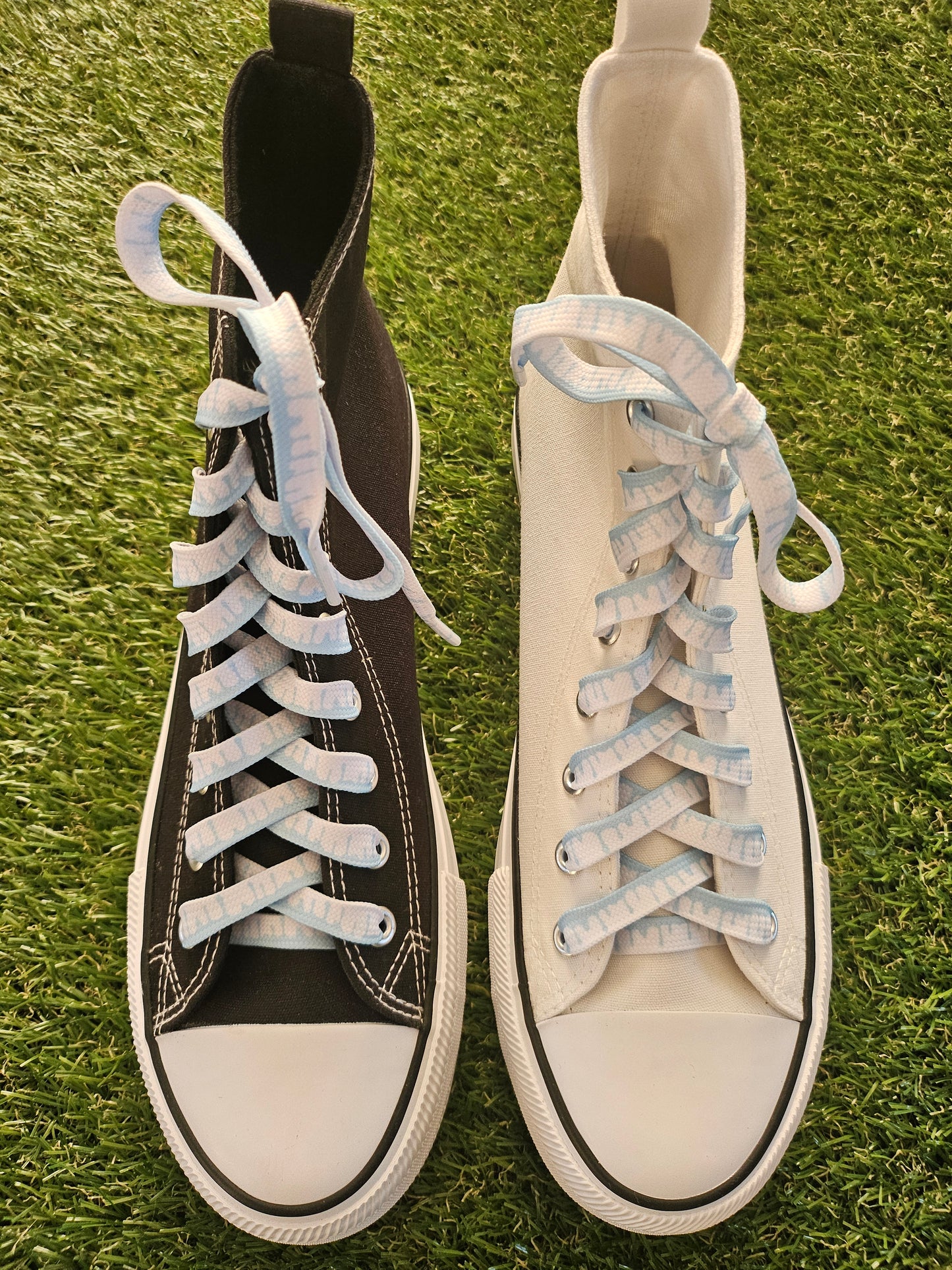 Two pairs of sneakers, one white and one black, with white and pale blue laces on a grass background.