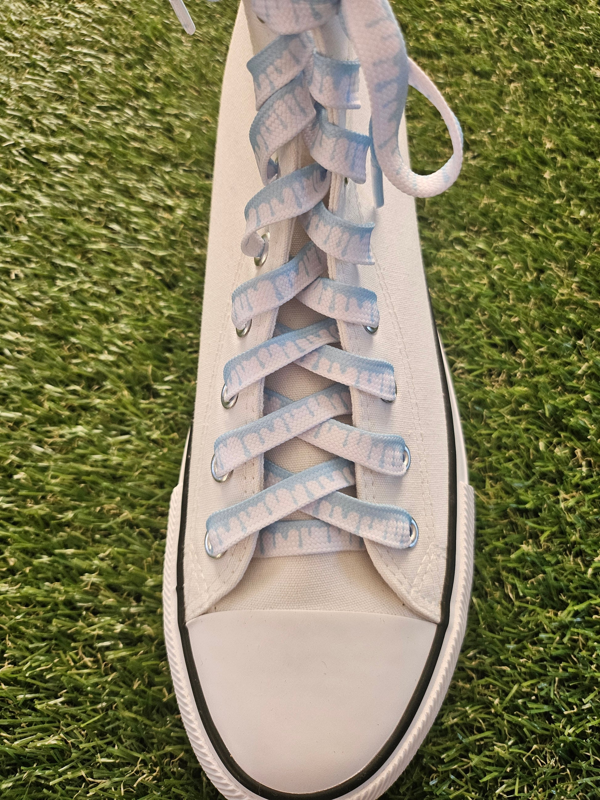 White sneaker with blue laces on grass