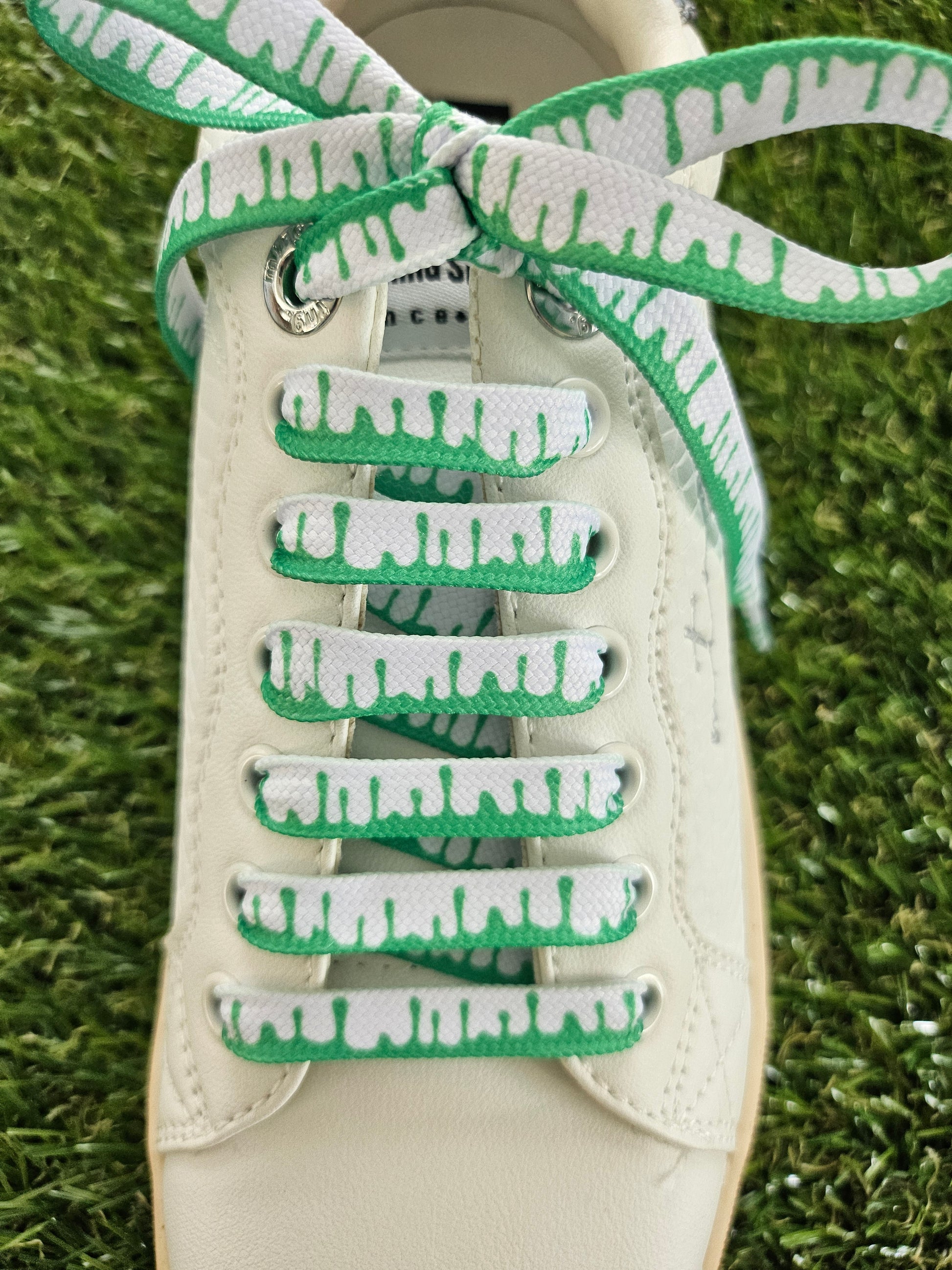 White sneaker with green and white patterned laces on a grass background