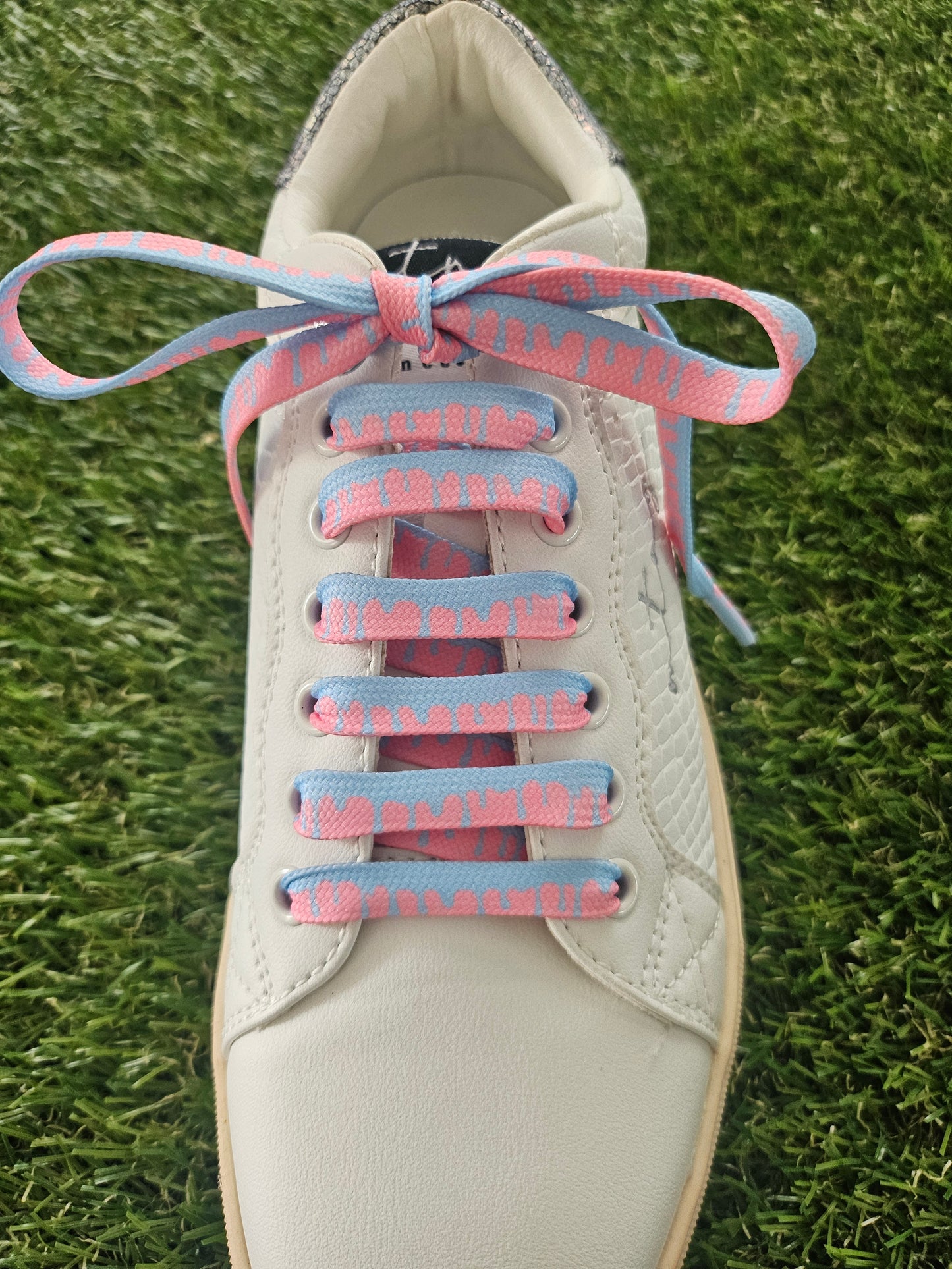 White sneaker with pink and blue shoelaces on a grass background