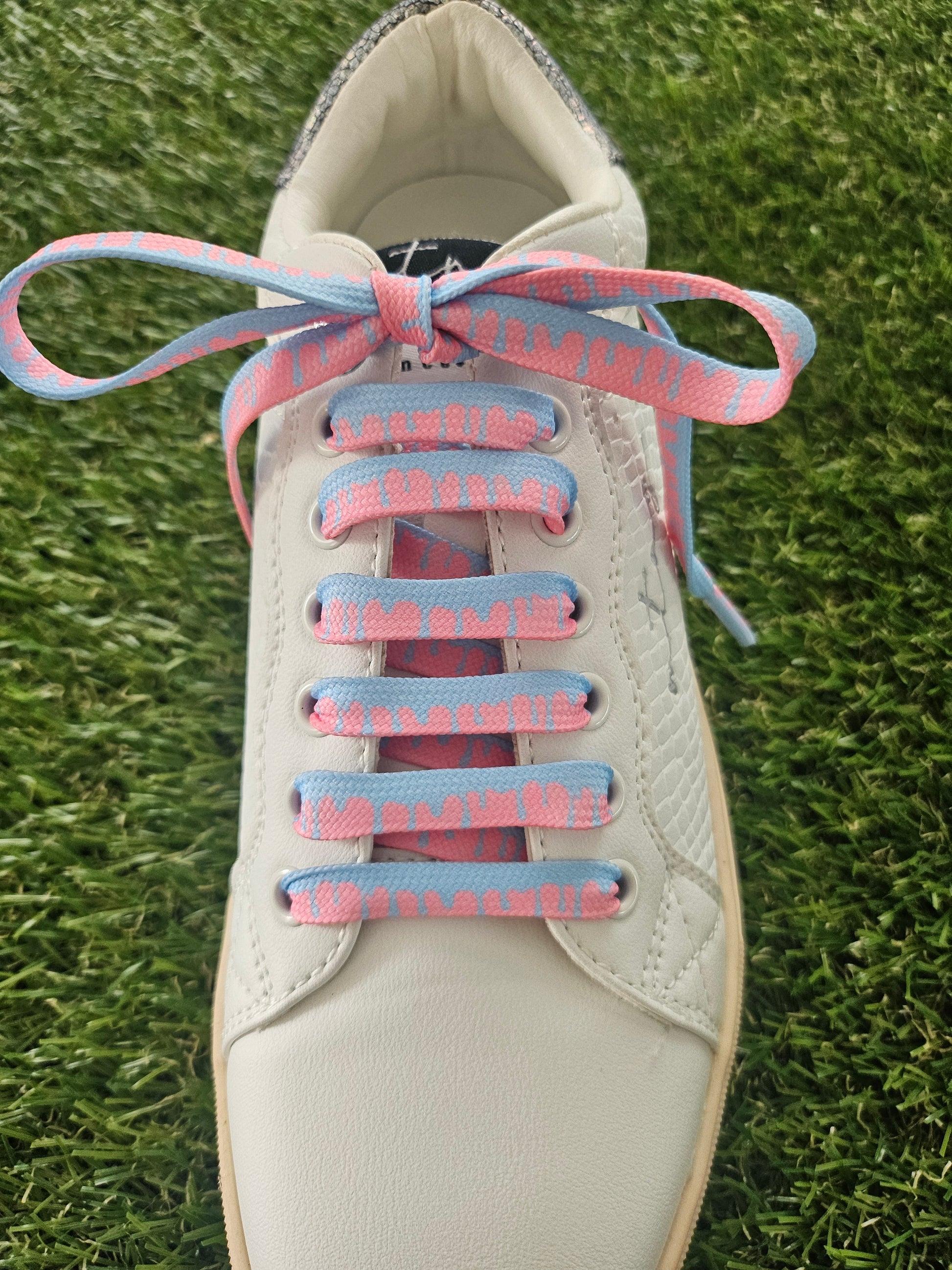 White sneaker with pink and blue shoelaces on a grass background