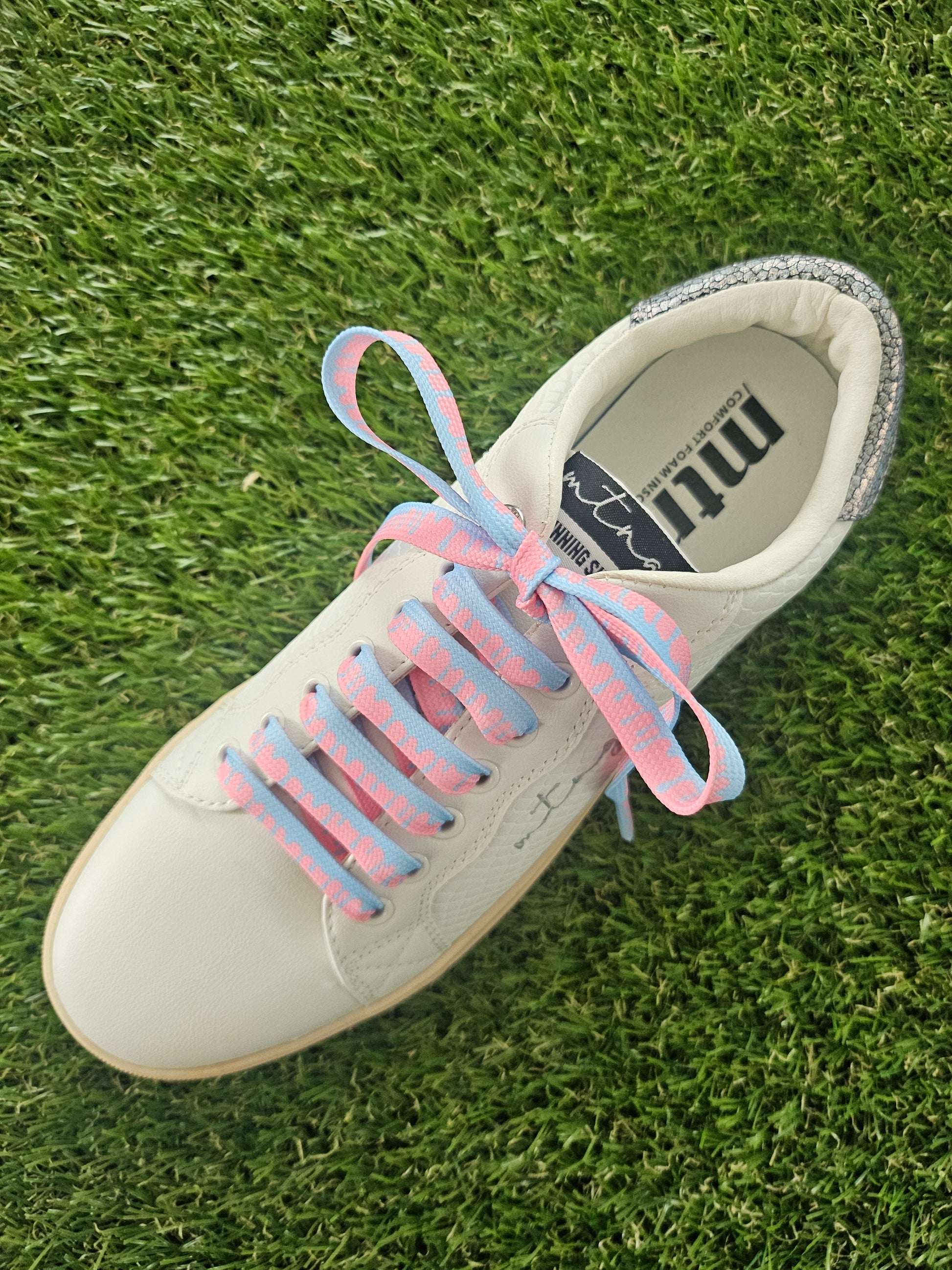 White sneaker with pink and blue shoelaces on grass