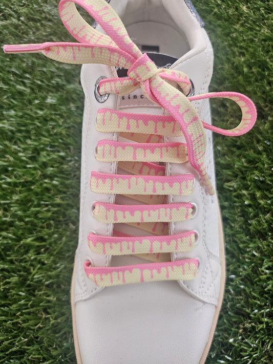 White sneaker with pink and yellow striped shoelaces on grass
