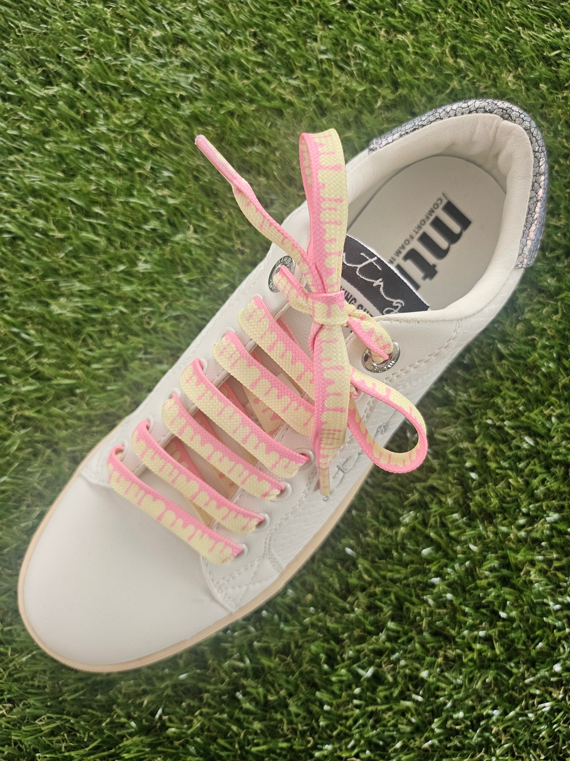 White sneaker with pink and yellow laces on grass