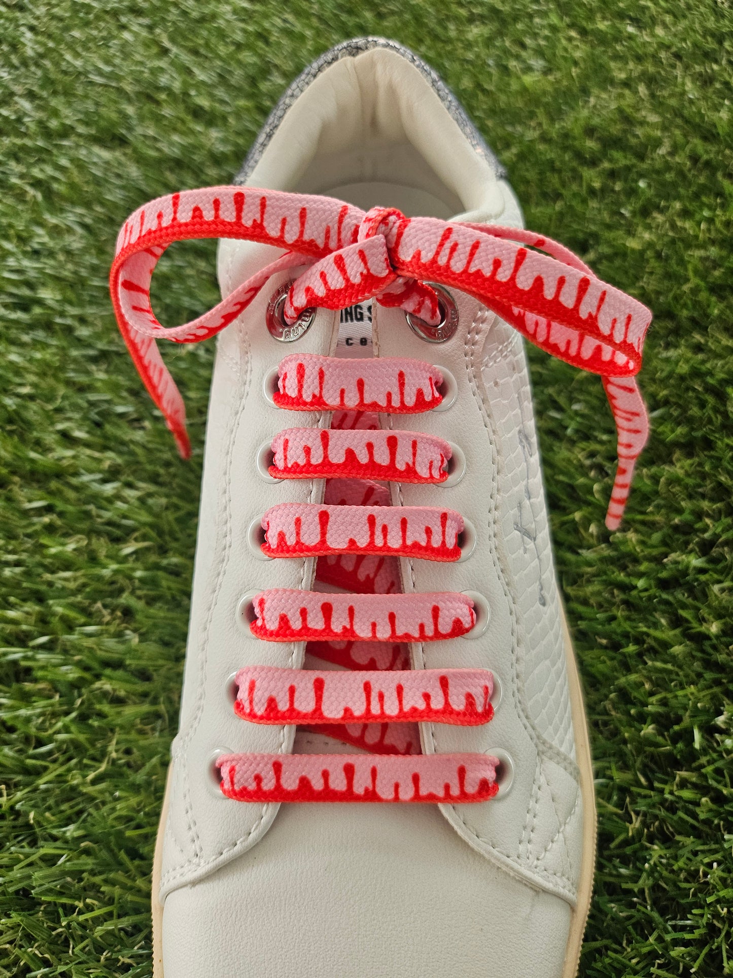 White sneaker with red laces on a grass background
