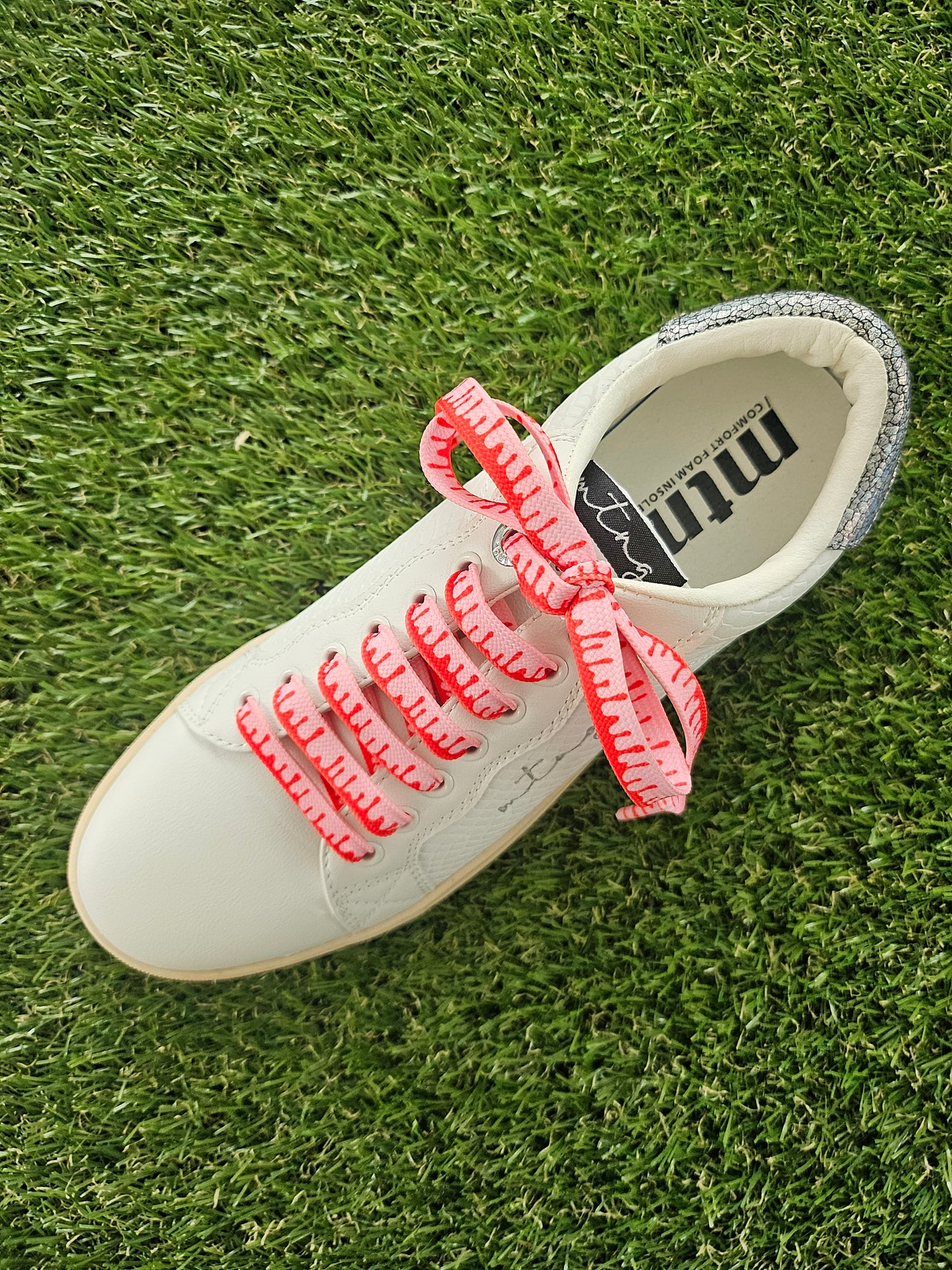 White sneaker with pink shoelaces on grass