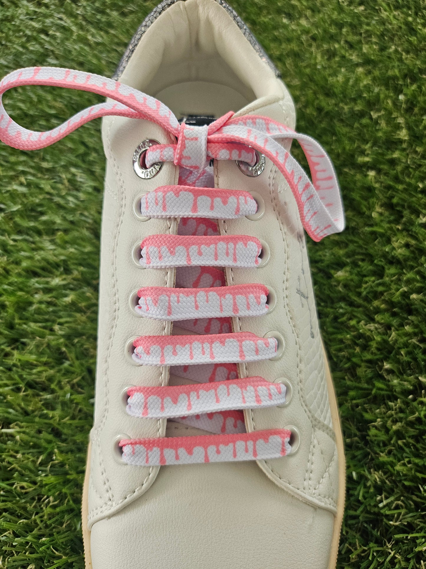 White sneaker with pink shoelaces on a grass background