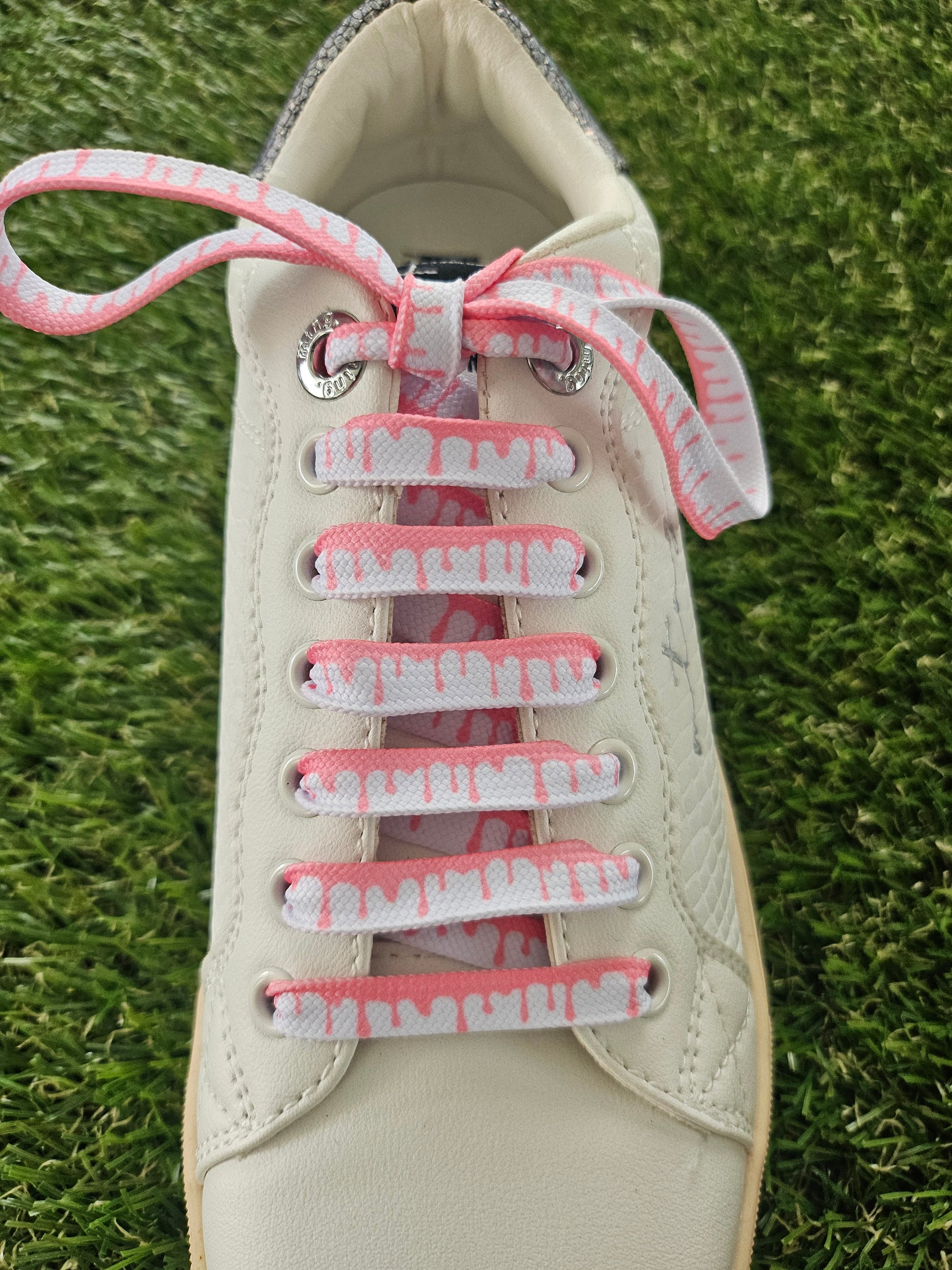 White sneaker with pink shoelaces on a grass background