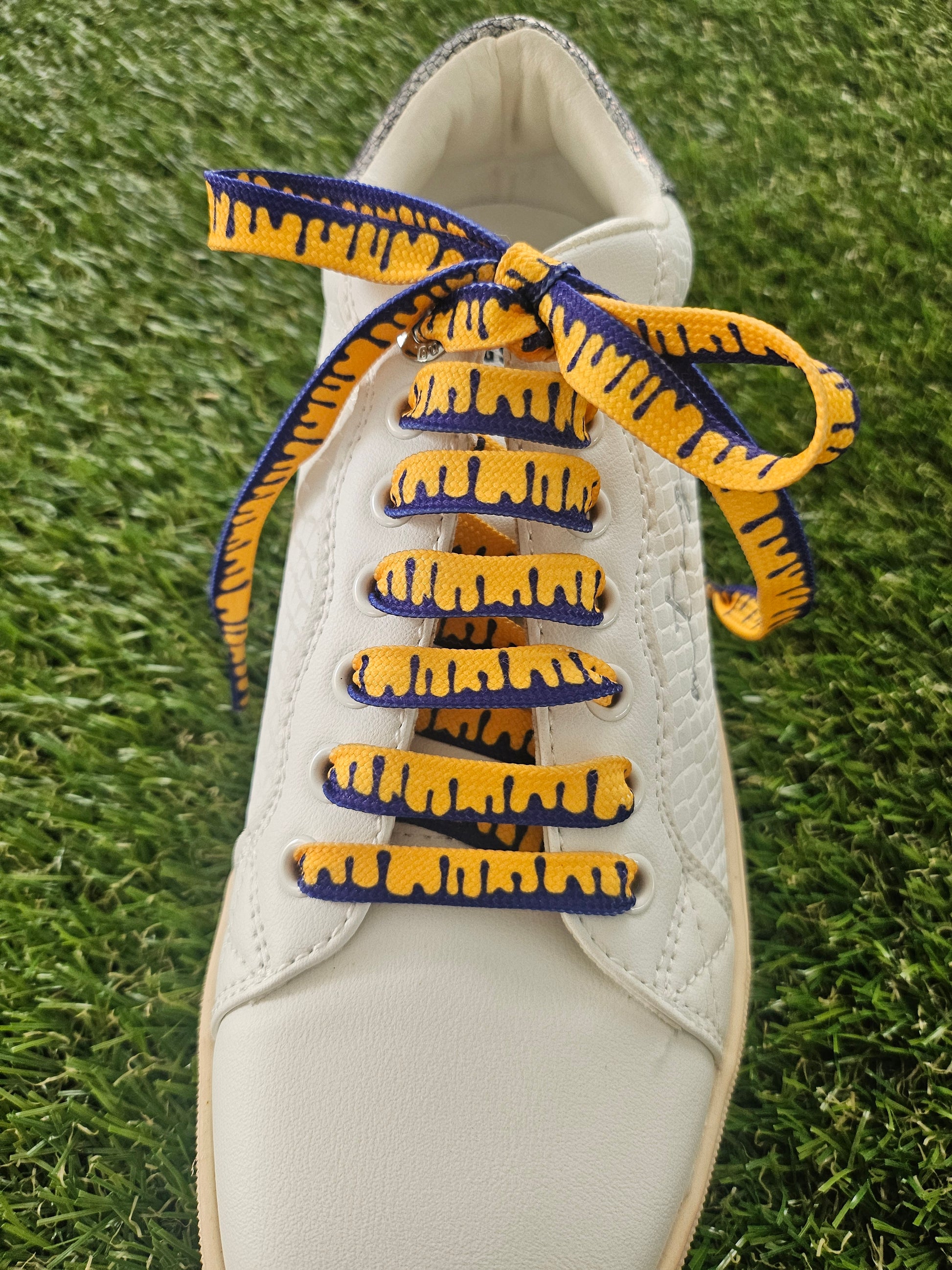 White sneaker with blue and yellow laces on a grass background