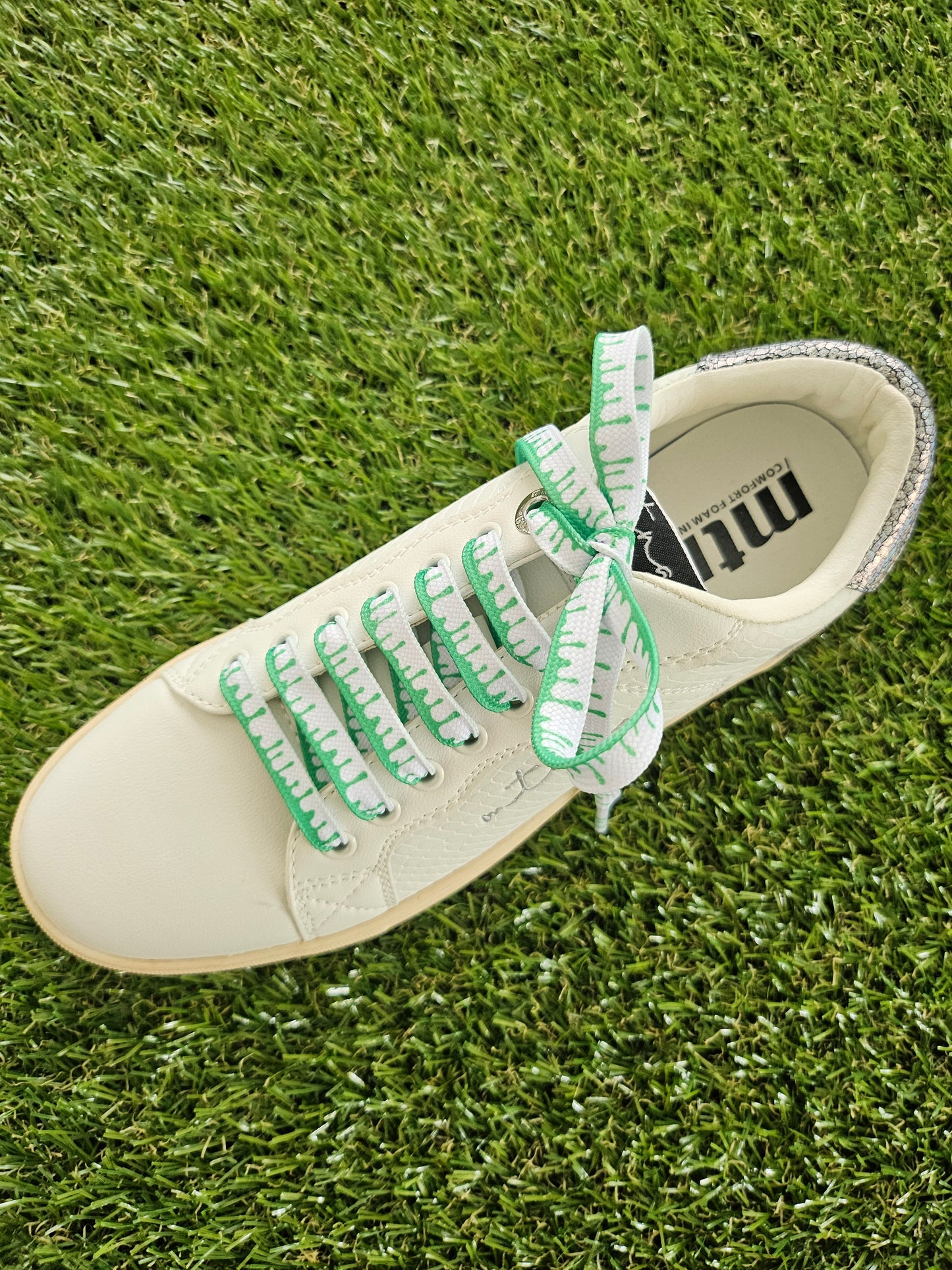 White sneaker with green laces on grass