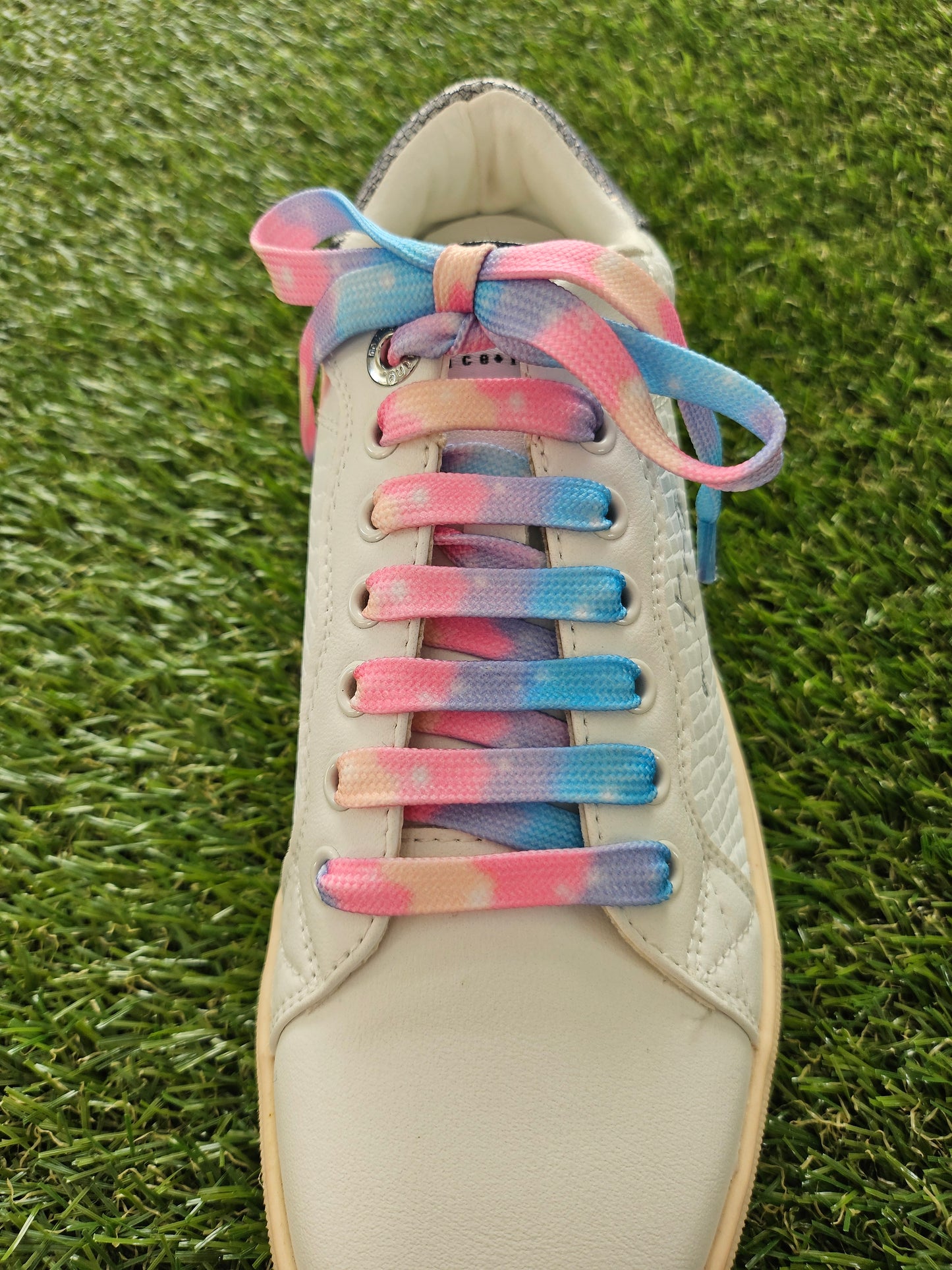 white trainer with colorful gradient laces on a grass background