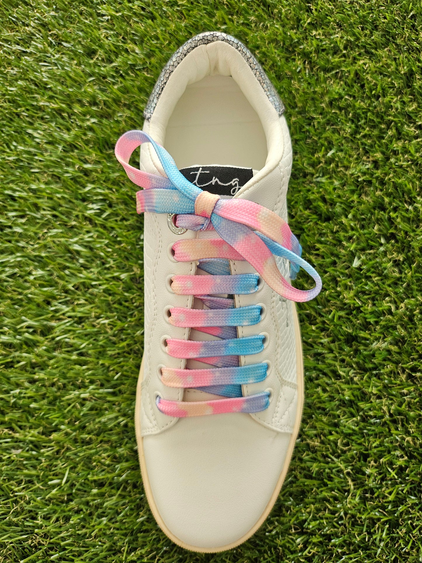 White sneaker with colorful pastel shoelaces on a grass background